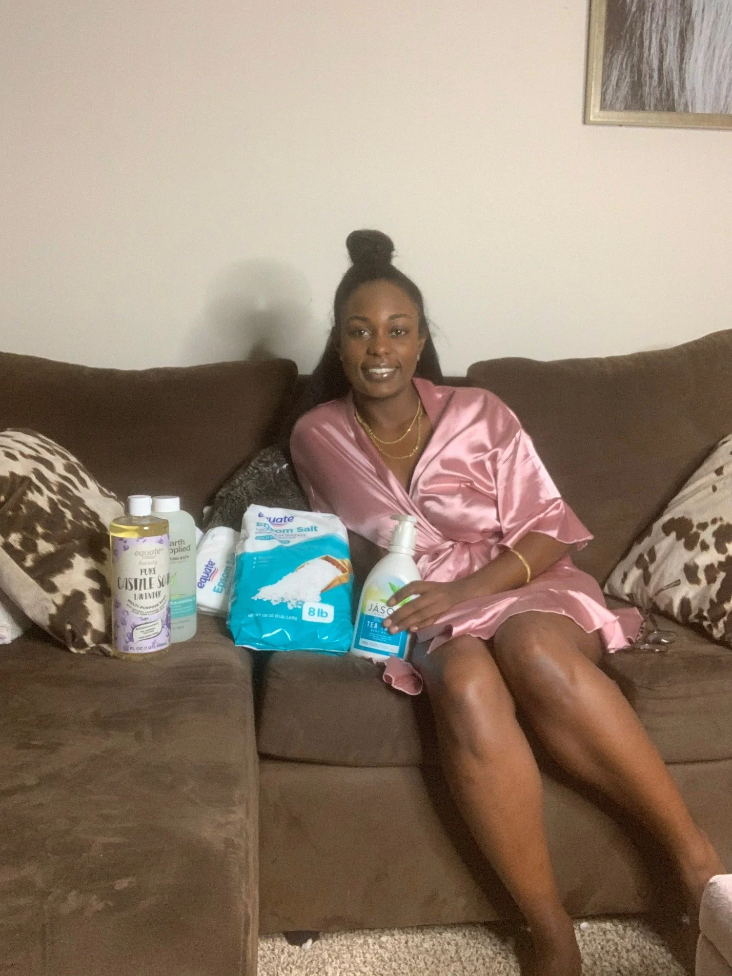 Brielle in a pink robe on the couch with her self care haul