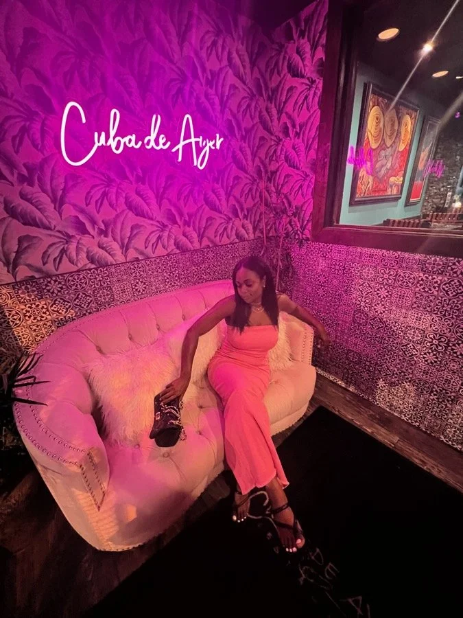 Brielle in a pink dress on a neon lit velvet sofa at a restaurant