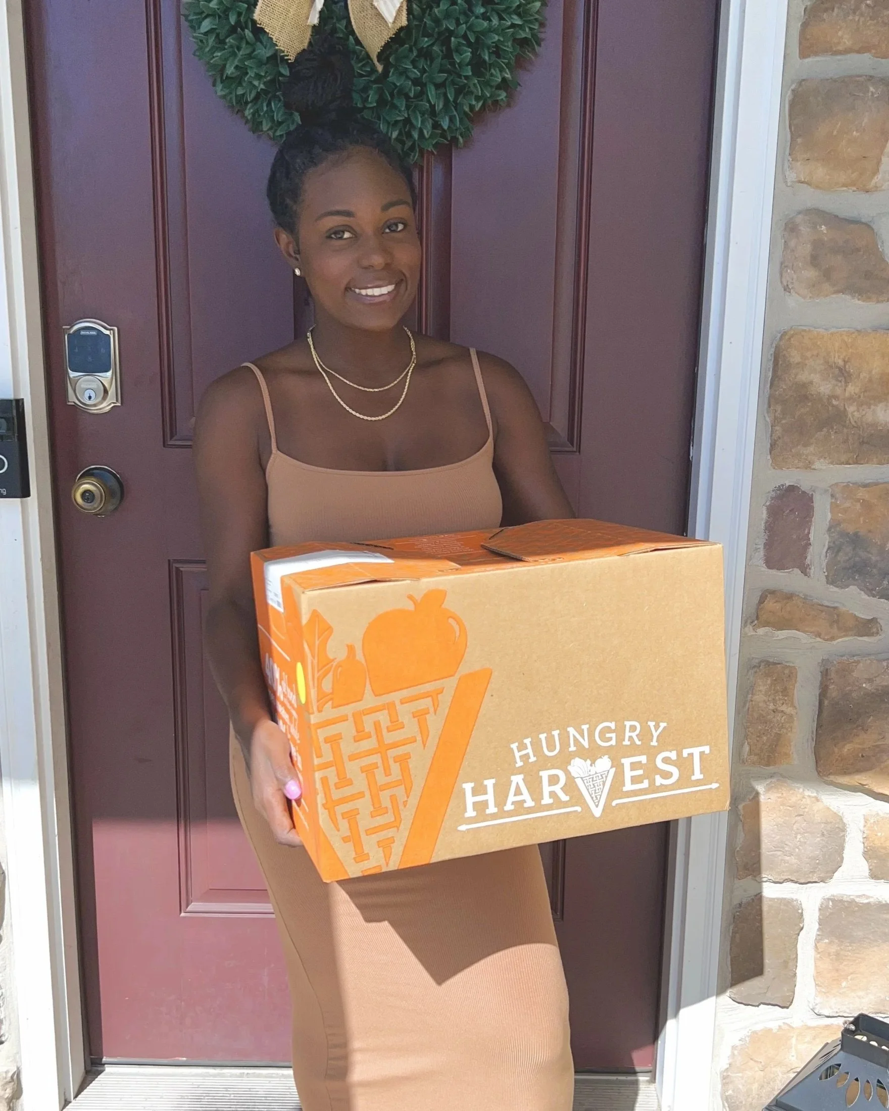Brielle smiling at her front door holding a delivery box