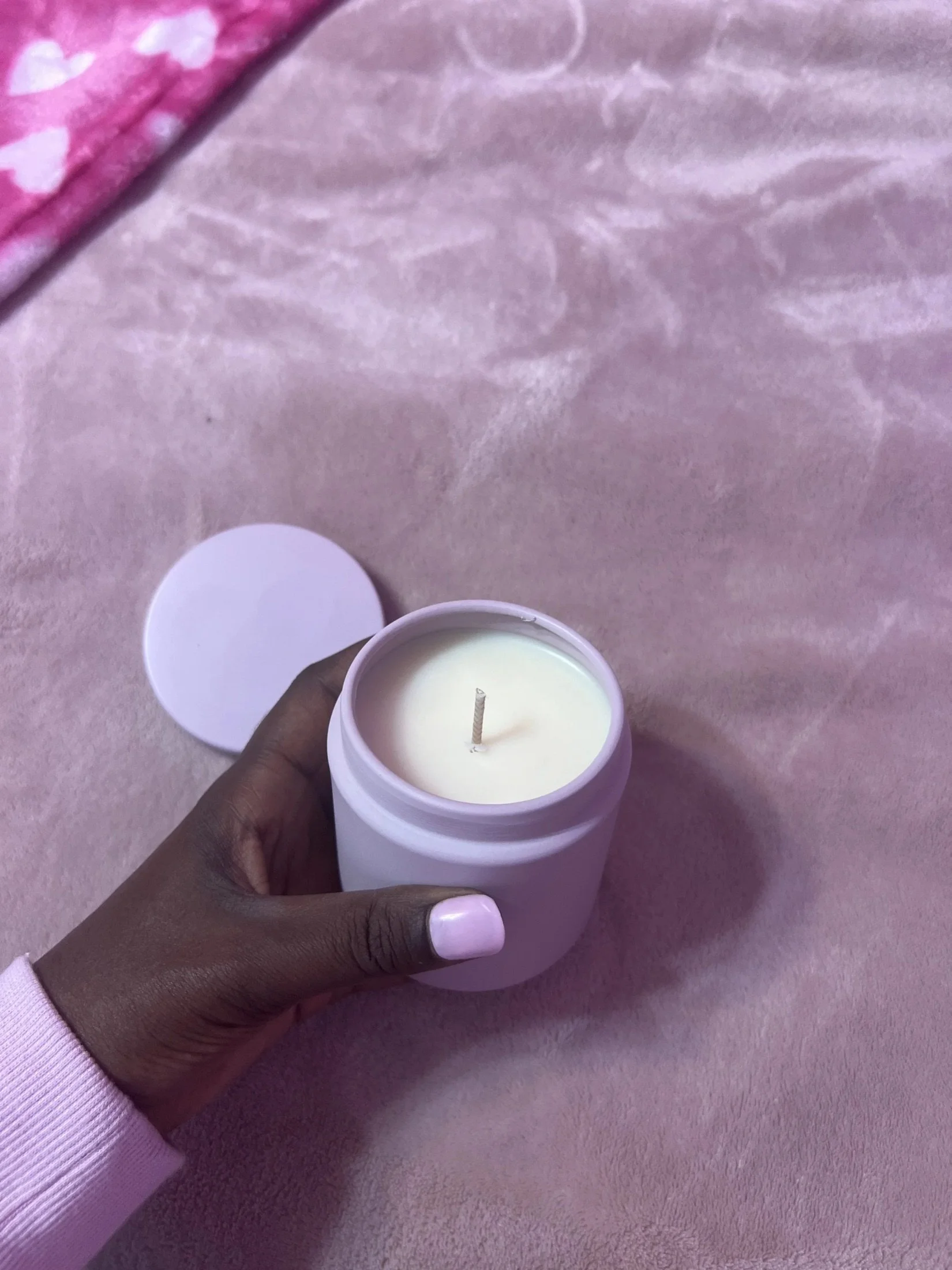 Hand holding a white candle over pink satin