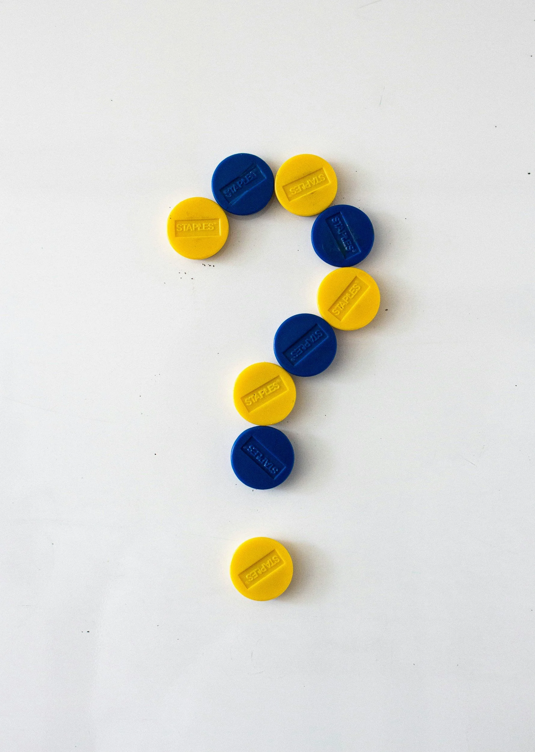 Yellow and blue Staples pharmacy pills arranged to form a question mark on a white surface.