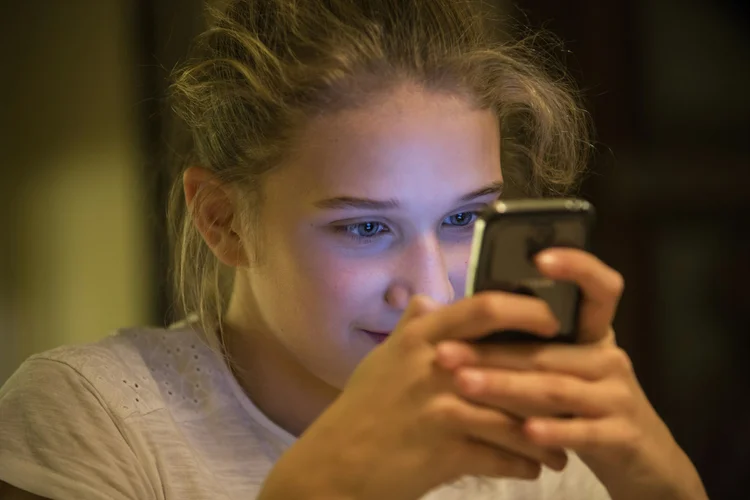 A person alone, illuminated only by a phone screen in a dark room