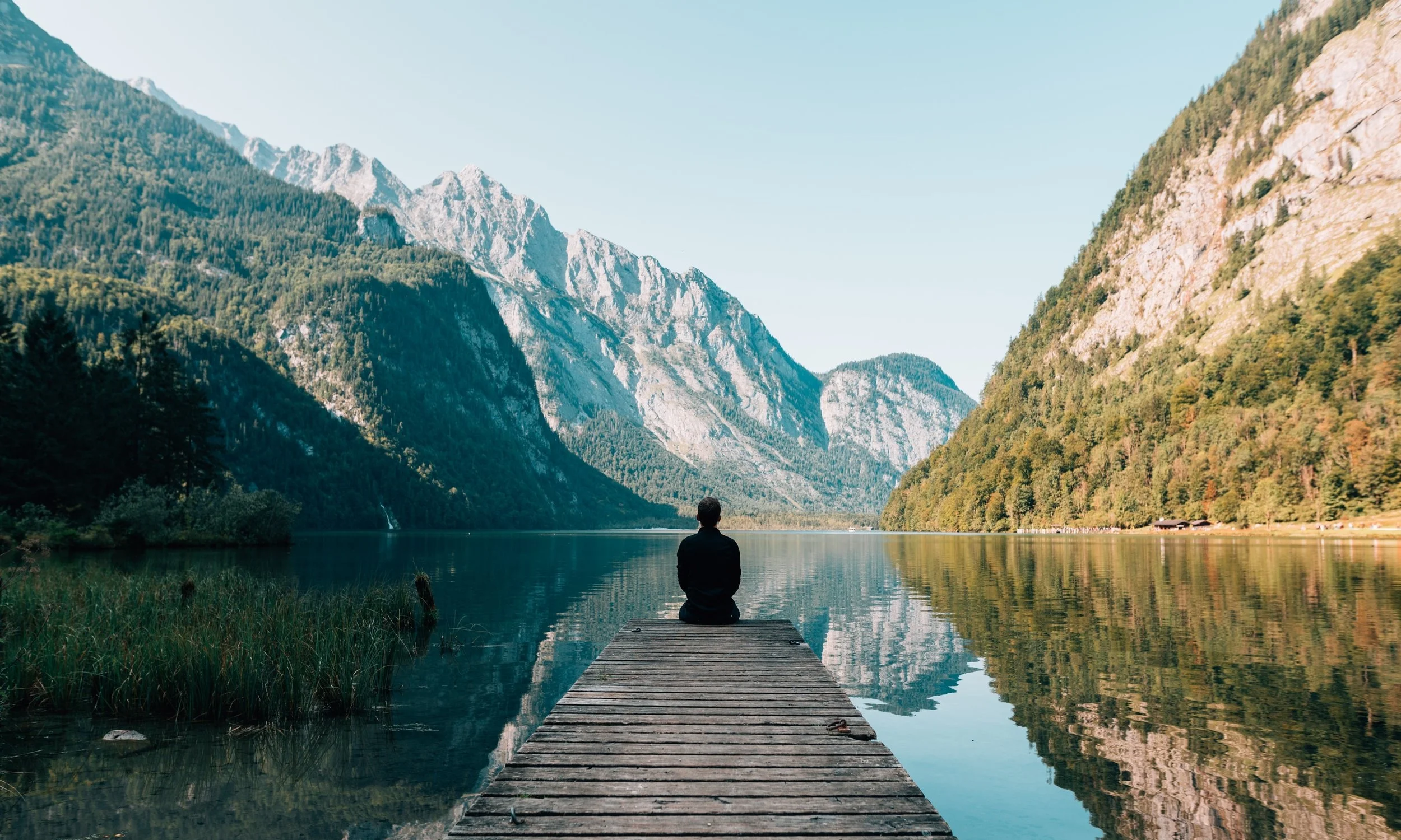Person sitting on a pier facing a dramatic mountain and lake scene