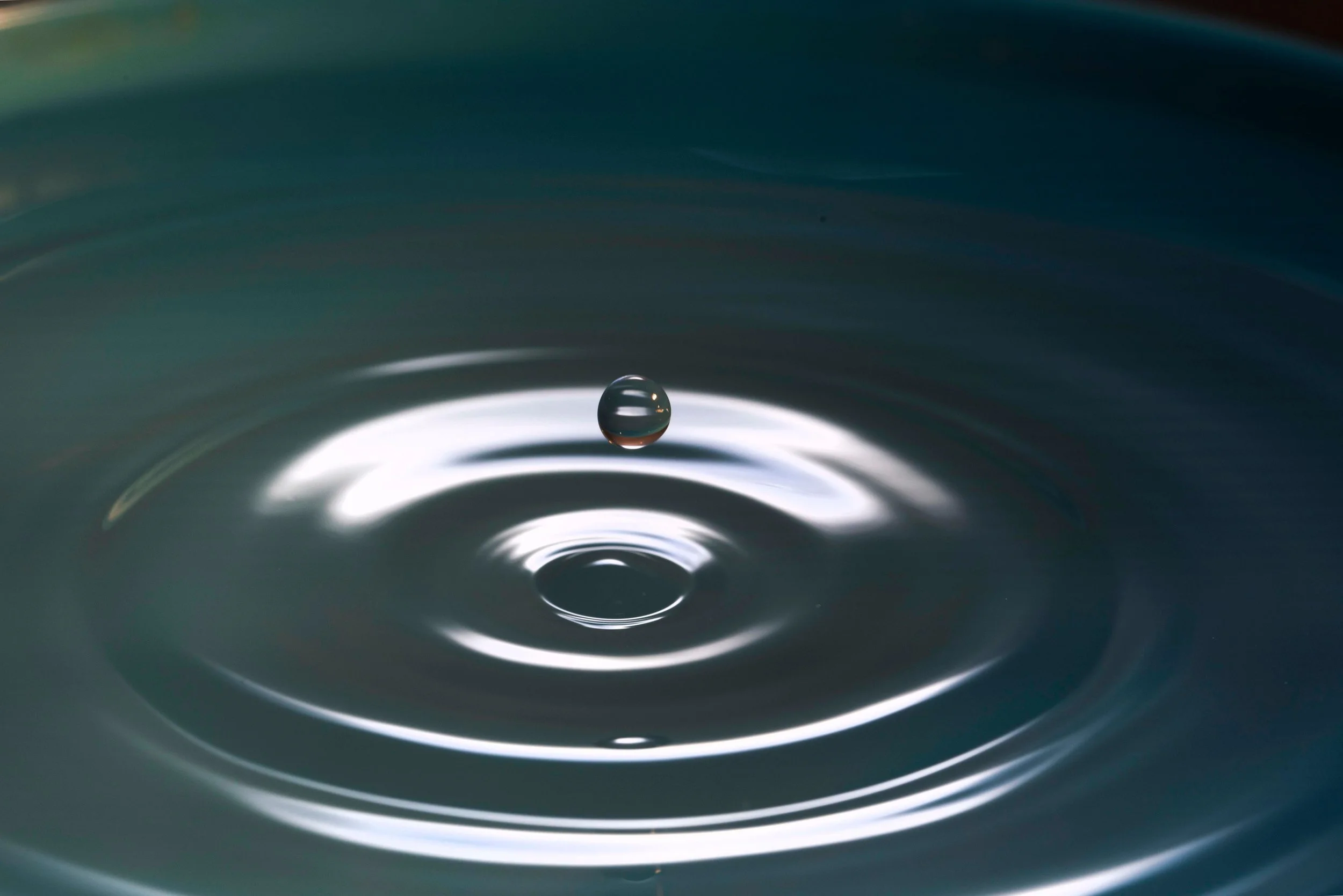 Image of a water droplet hitting the surface of water causing ripples