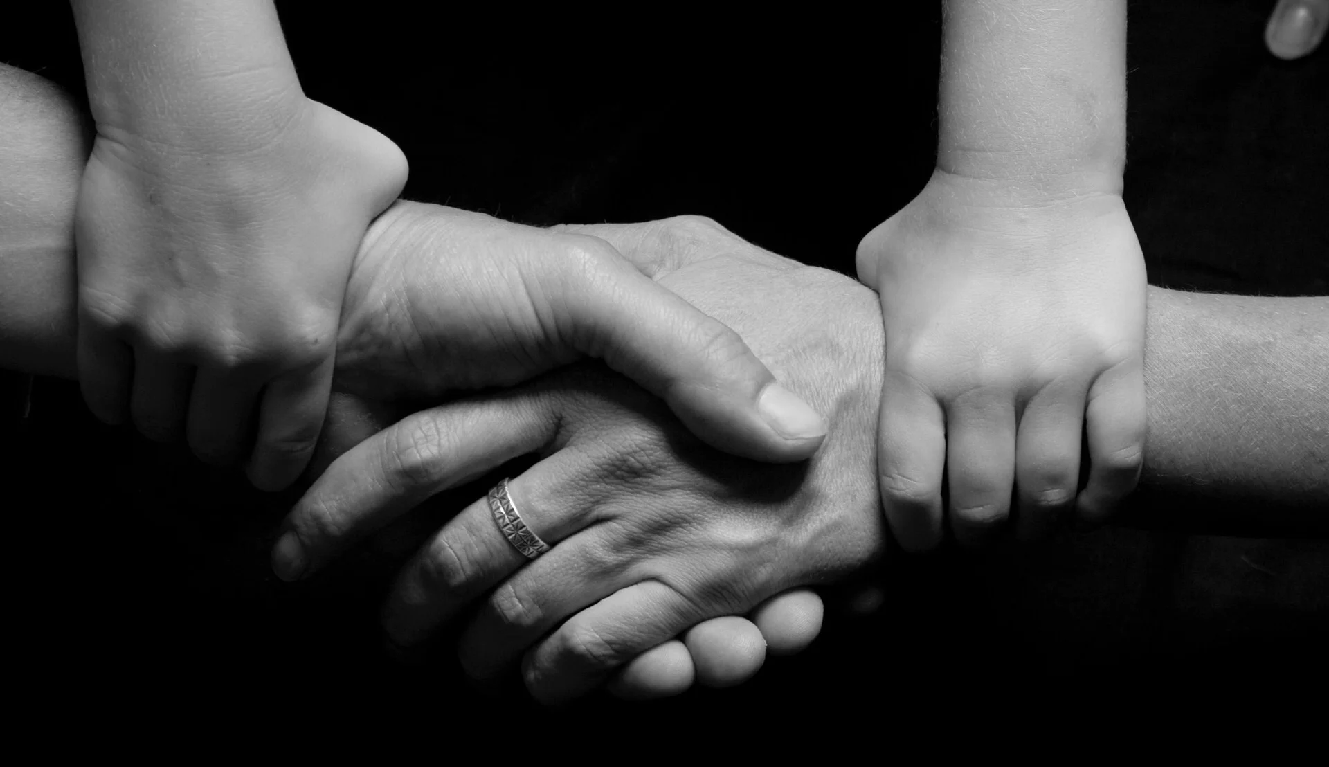 Black and white photo of two adult arms holding hands with smaller children's arms grasping the wrist of the adult arms