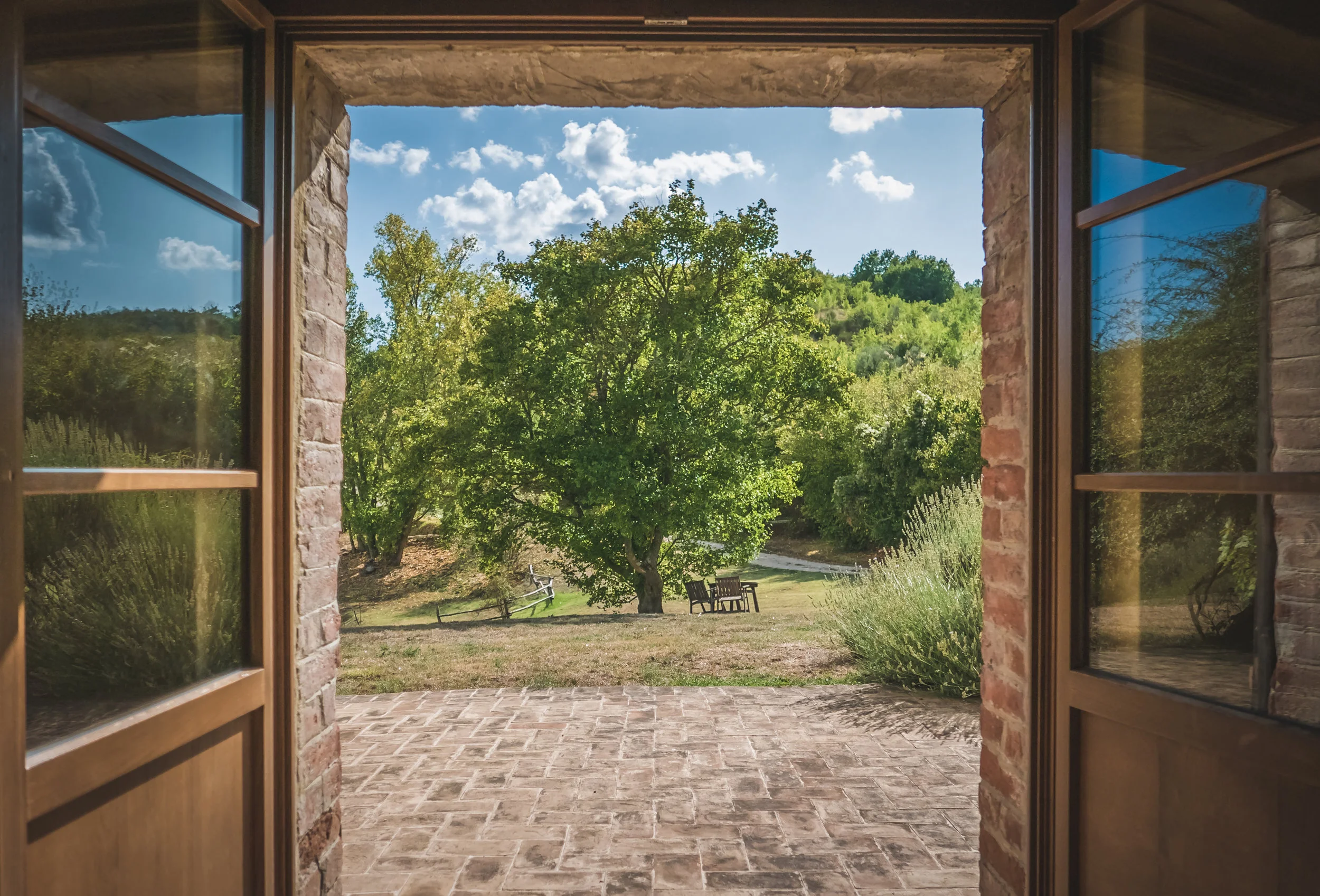Photo looking through an open doorway into the garden of a home with trees, stone pavers and benches
