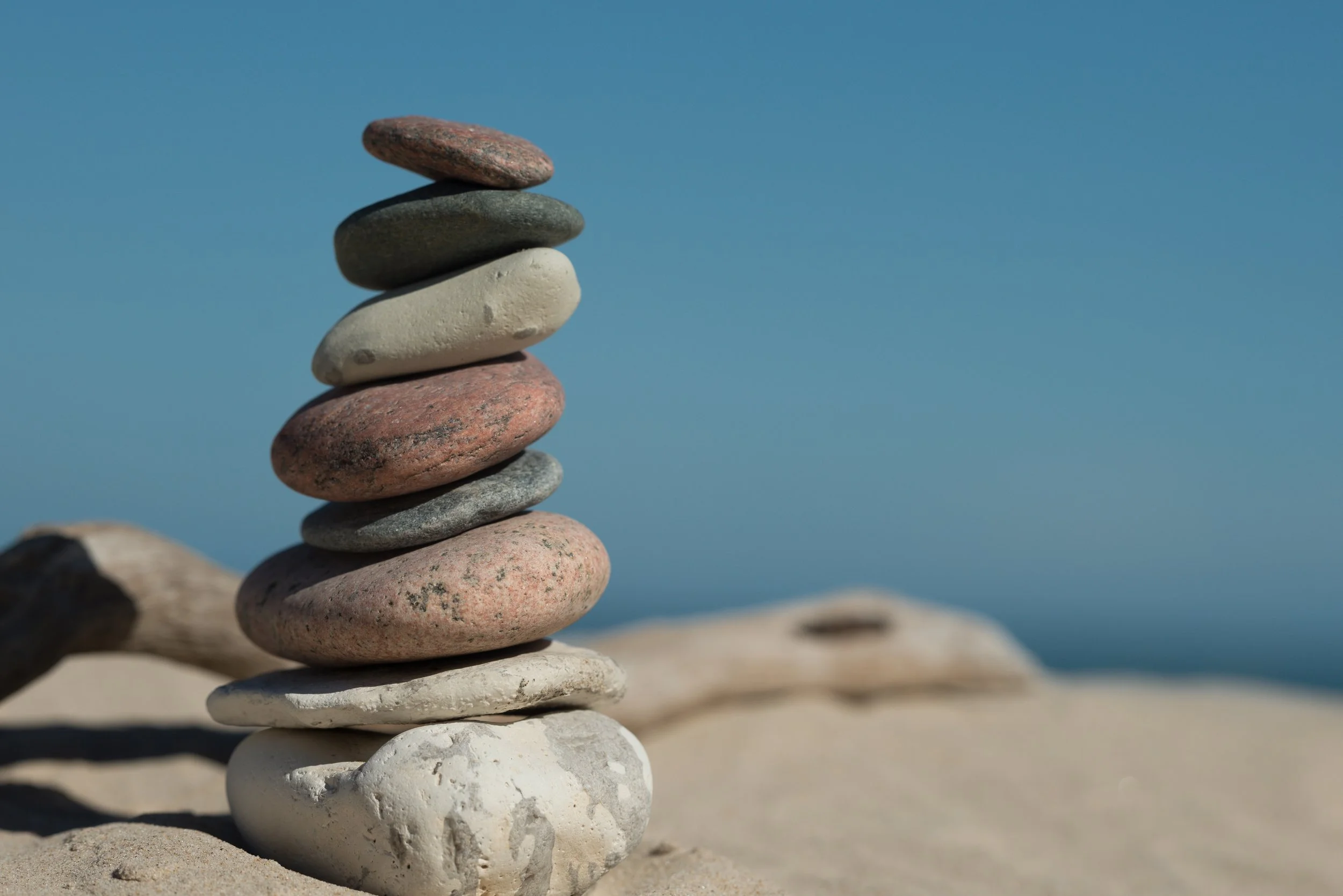 Photo of eight large stacked stones with the smallest stone on top against a blue and sand colored background
