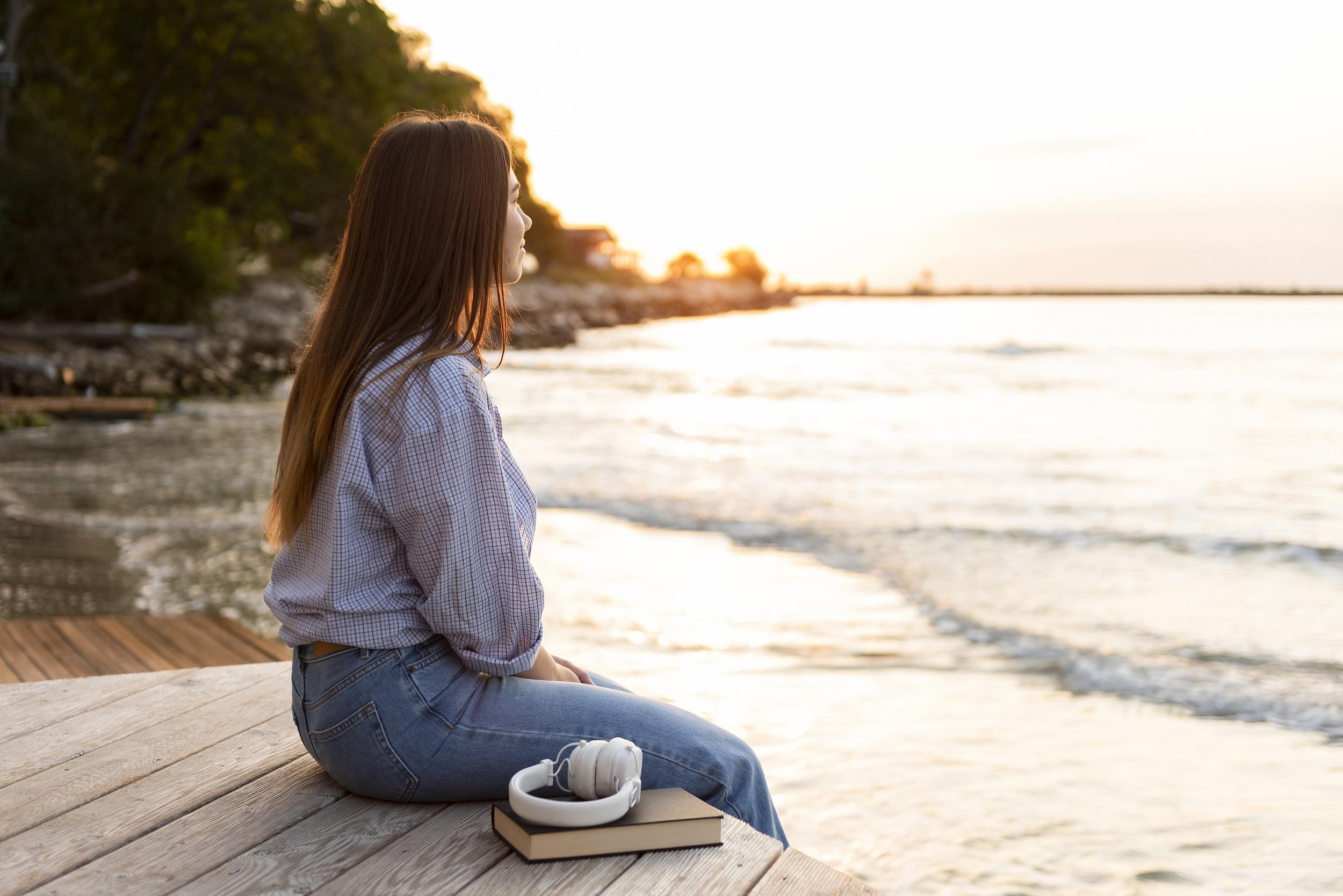 Photo of a young woman sitting on a wooden deck along the shore of a body of water