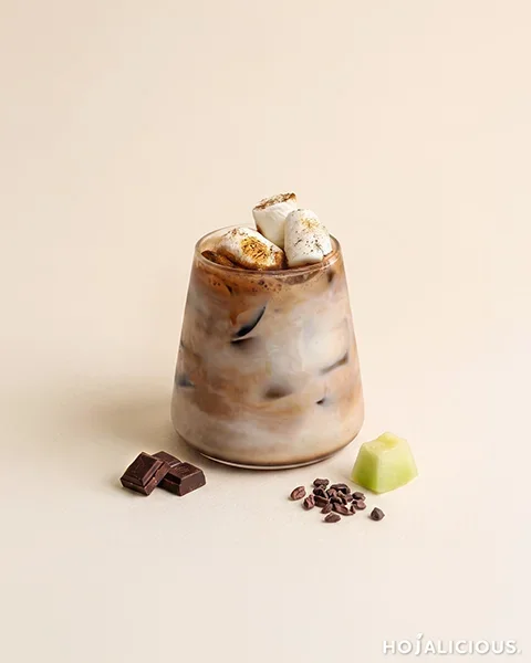 Vanilla Honeydew Cocoa made with honeydew flavor jam, vanilla syrup, fresh milk, premium Belgian cocoa powder, warm water, marshmallows, and ice, featuring a layered iced cocoa drink topped with toasted marshmallows.