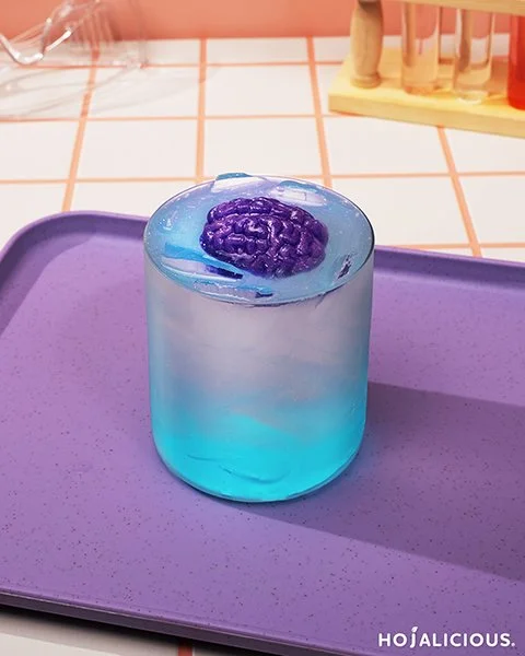 Galaxy Brain Sparkle drink with cotton candy syrup base, lemon sparkling water, floating purple brain jelly, and silver mica powder topping.