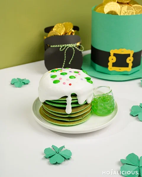 Fluffy green matcha pancakes stacked with cream cap, whipped cream, and colorful sprinkles for a festive café-style dessert