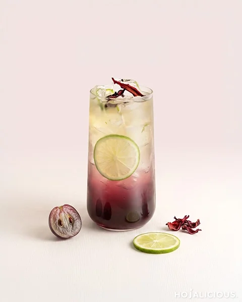 Grape Hibiscus Tea made with Golden Mountain Tea Base, Grape Syrup, Hibiscus Syrup, fresh lemon slices, and dried hibiscus flowers, featuring a vibrant purple gradient and refreshing floral fruit tea flavor.