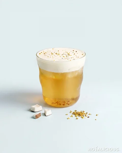 Osmanthus Coconut Cloud Tea made with oolong tea, coconut water, osmanthus syrup, cane sugar syrup, coconut cream foam, ice, and dried osmanthus, featuring a golden coconut tea topped with white cream foam.