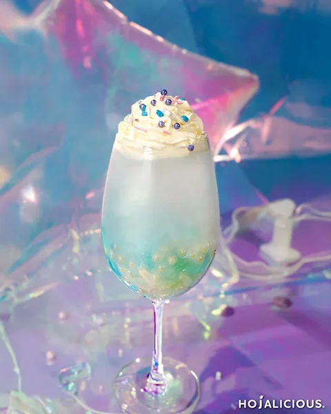 Galaxy blue popping boba drink with a layered blue gradient, bursting boba pearls, and whipped cream topping, photographed in a dreamy holographic backdrop for aesthetic blue drink inspiration.