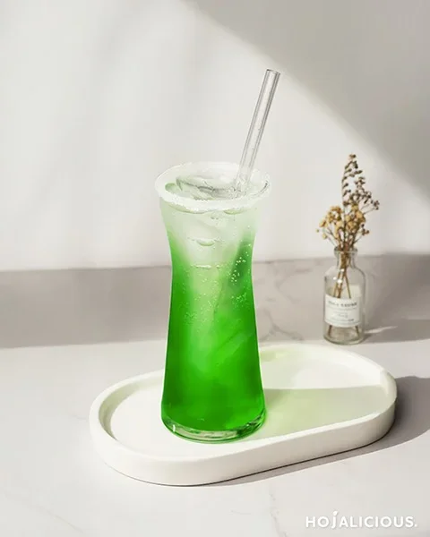 A bright green cocktail made with green apple, mint, vodka, and soda water, served with a salted rim and playful garnish.