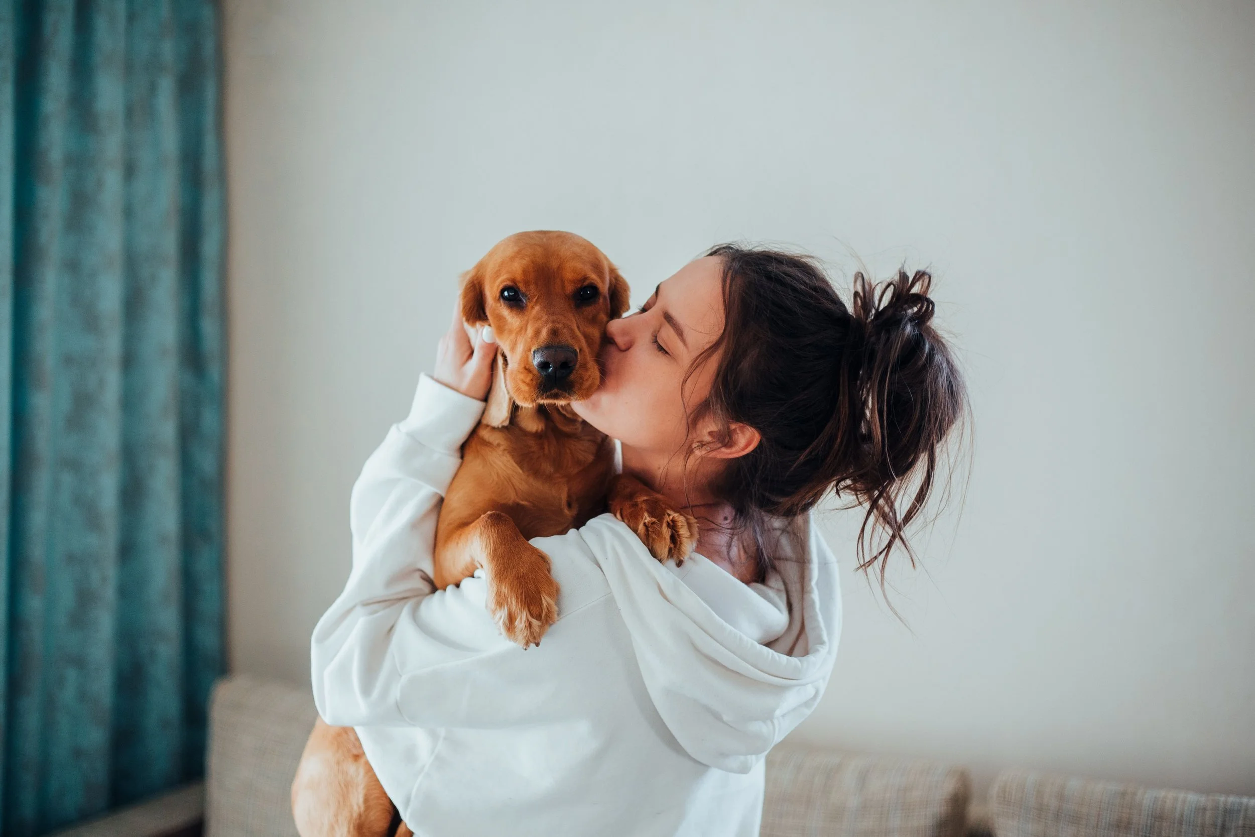 A young woman affectionately kisses her dog indoors.