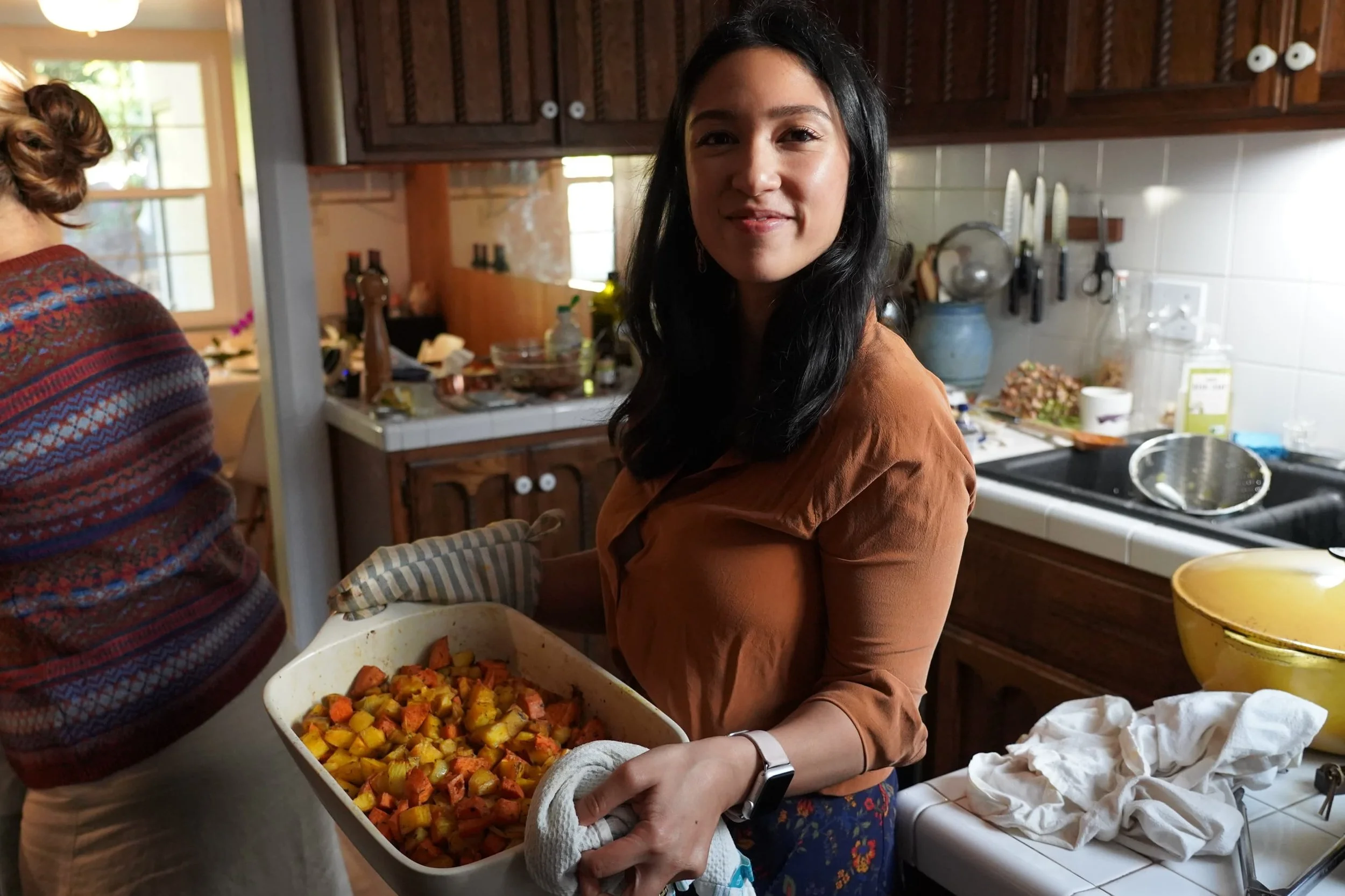 Nadia pulling some squashes and sweet potatoes out of the oven.