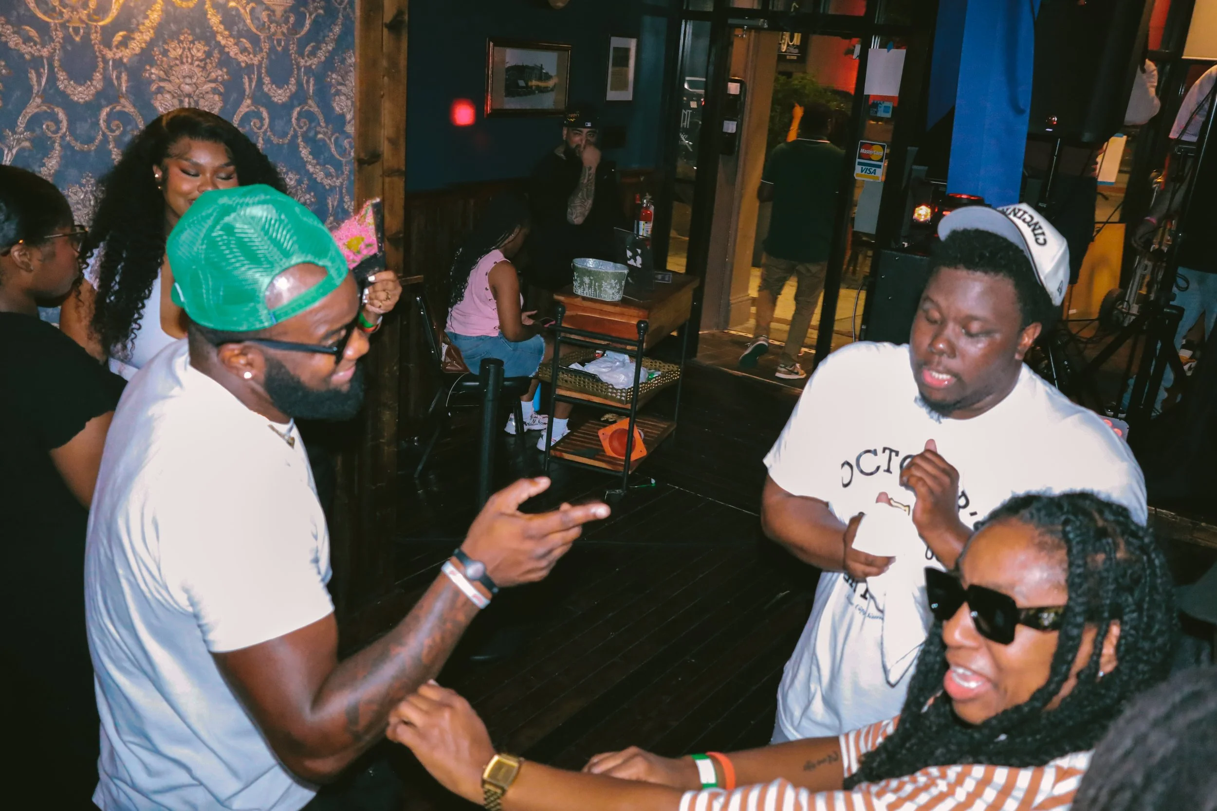 Group of young adults in a lively indoor setting, engaging in conversation and dancing, with some wearing casual clothing and accessories.
