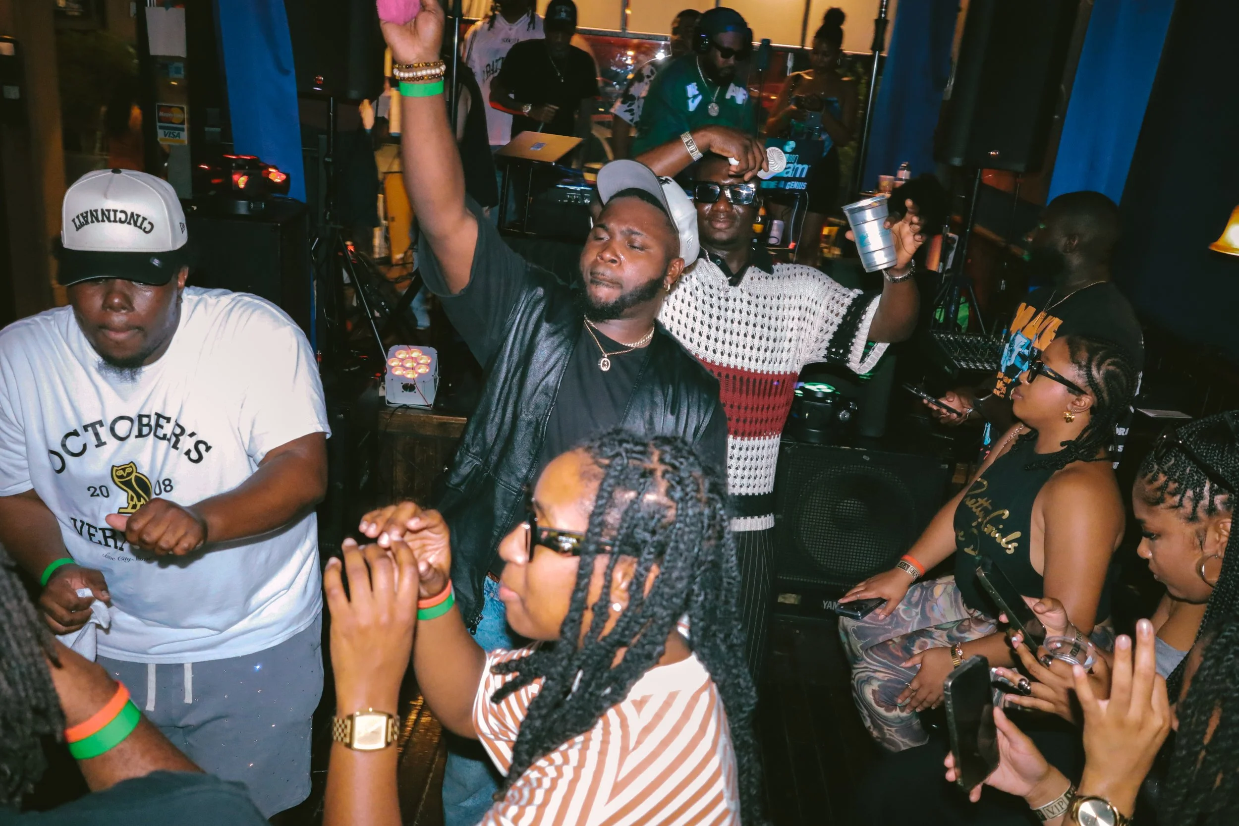 People dancing and socializing at a lively indoor party or club, with a DJ playing music in the background.