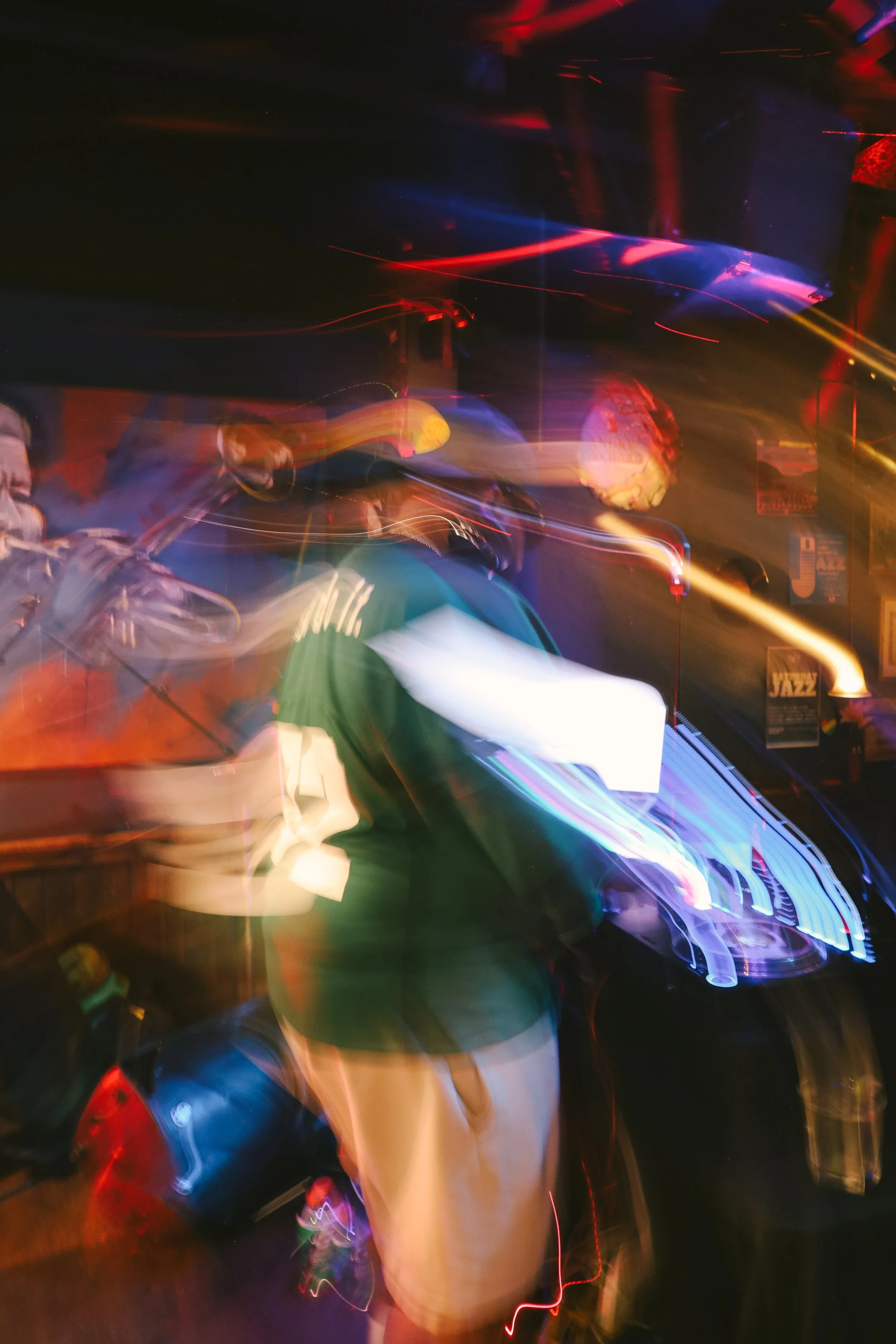 A person wearing a green shirt and beige shorts standing at a DJ booth with colorful light trails surrounding them.