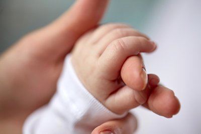 A baby's hand holding a mother's thumb