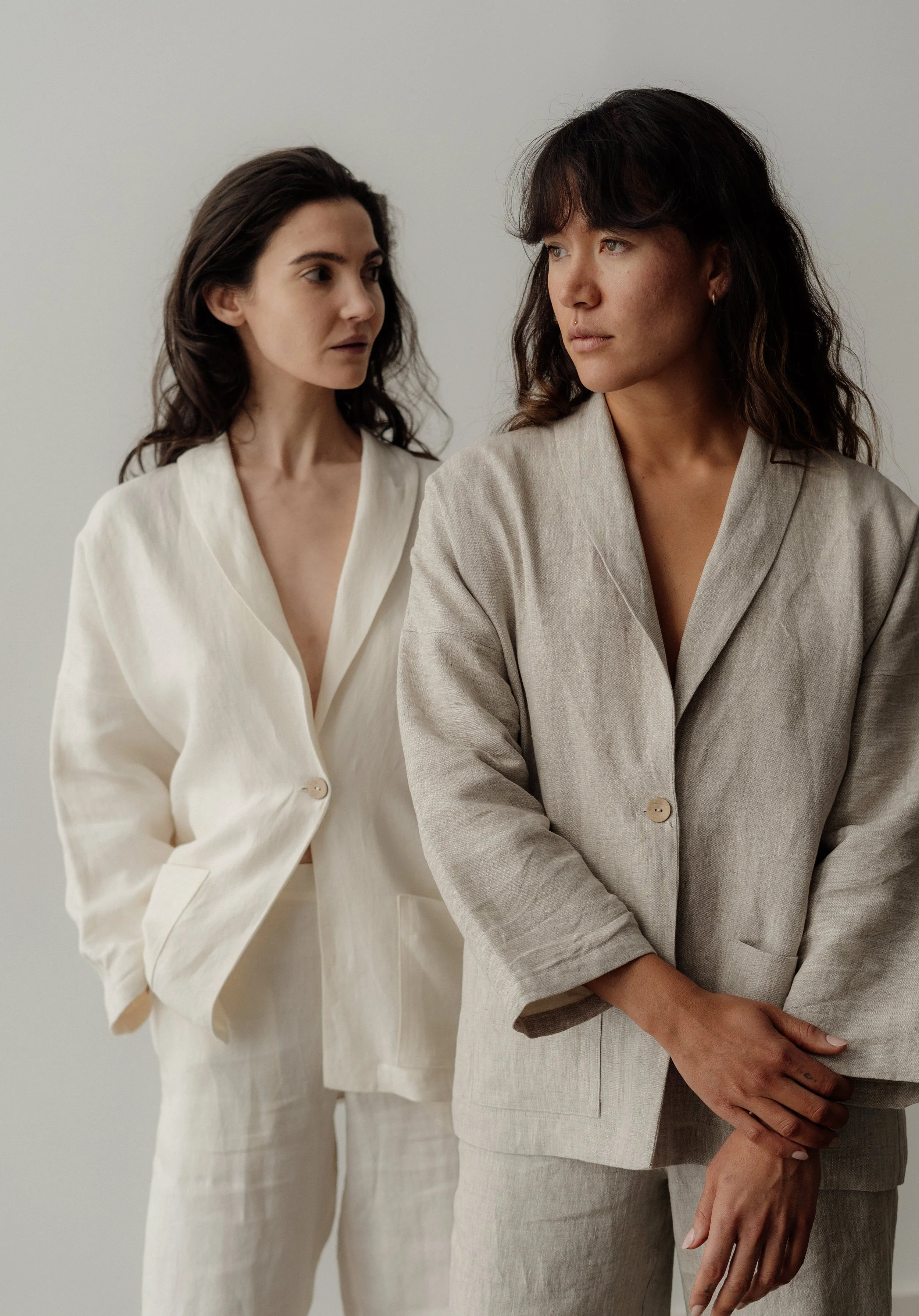 Two women wearing beige and cream-colored suits standing against a plain background