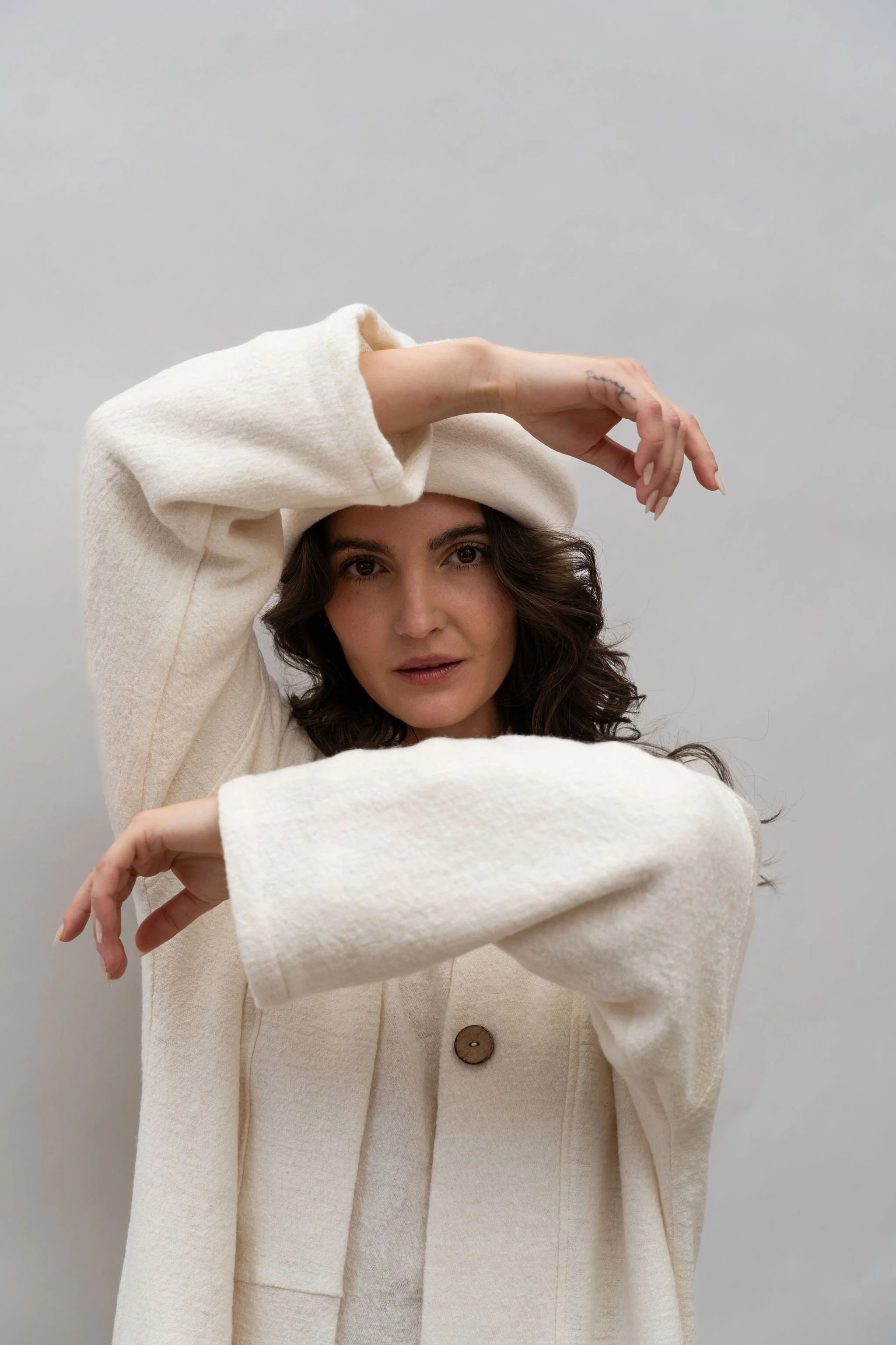 Close up front view of a woman wearing a wool coat in Vanilla with arms around face