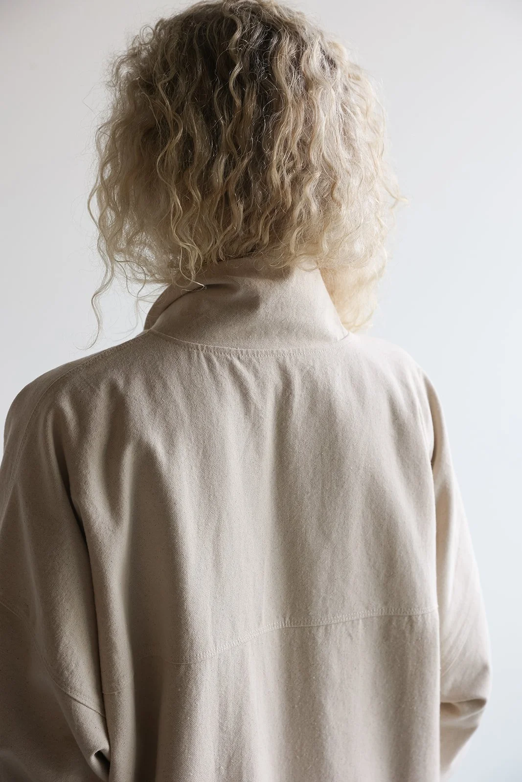 Close up back view of a woman wearing a canvas linen trench coat in Sand with collar popped up