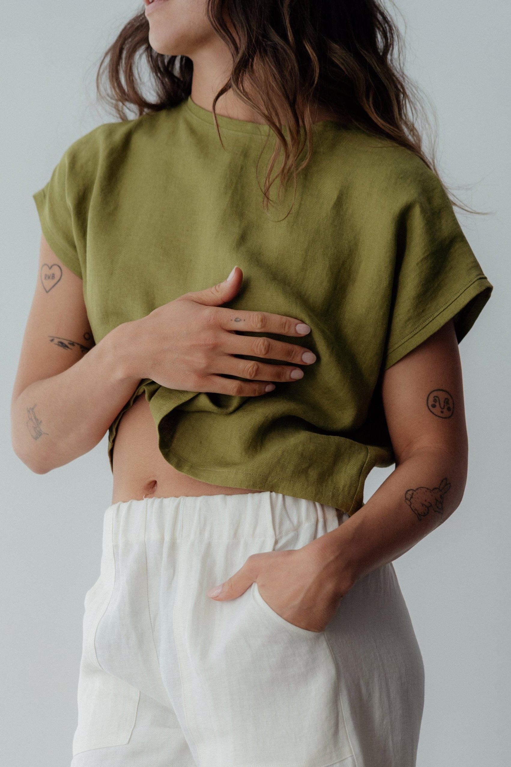 Woman wearing pesto green short sleeve linen top with right hand on chest
