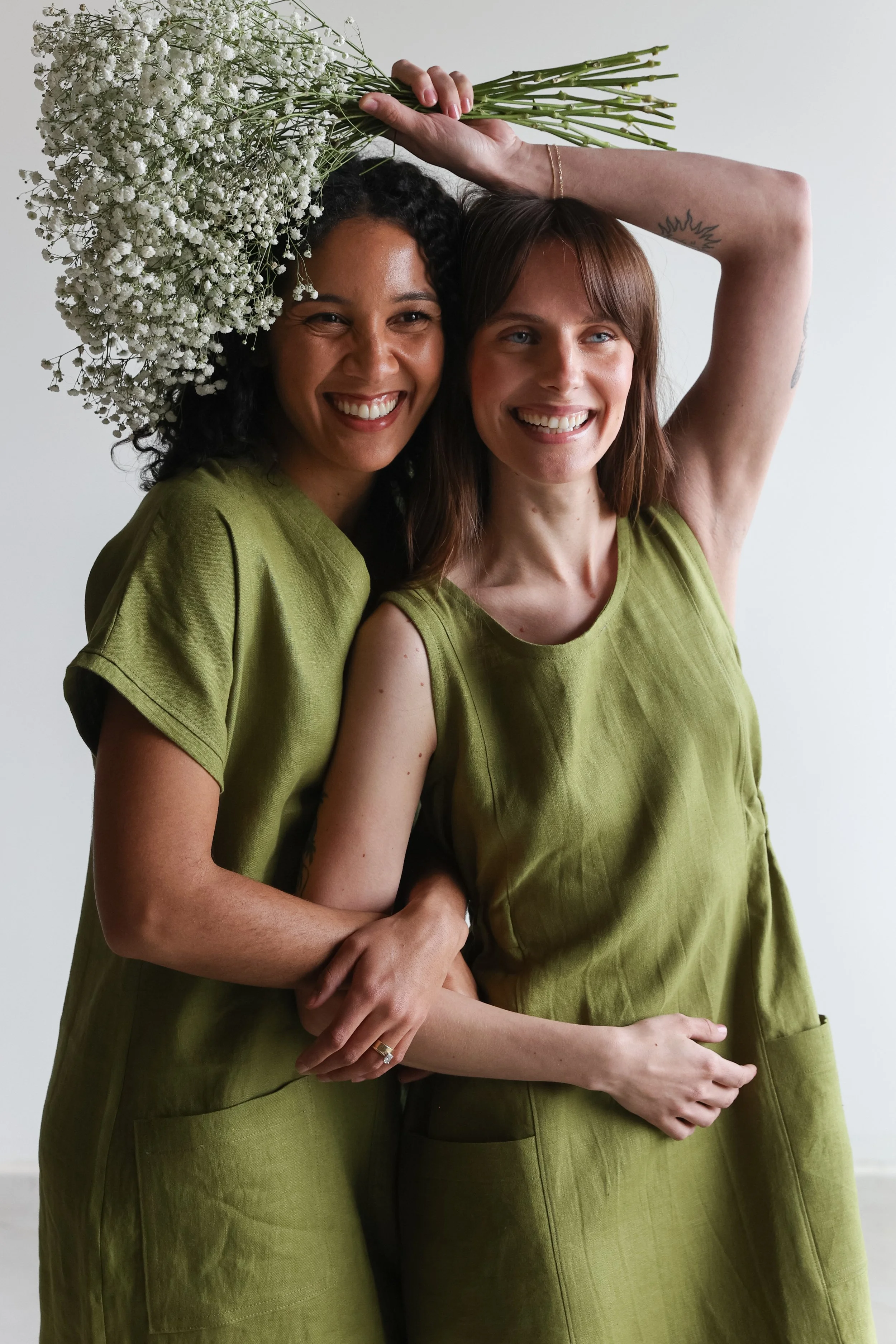 Two women smiling, one holding a large bouquet of white baby's breath flowers above her head.