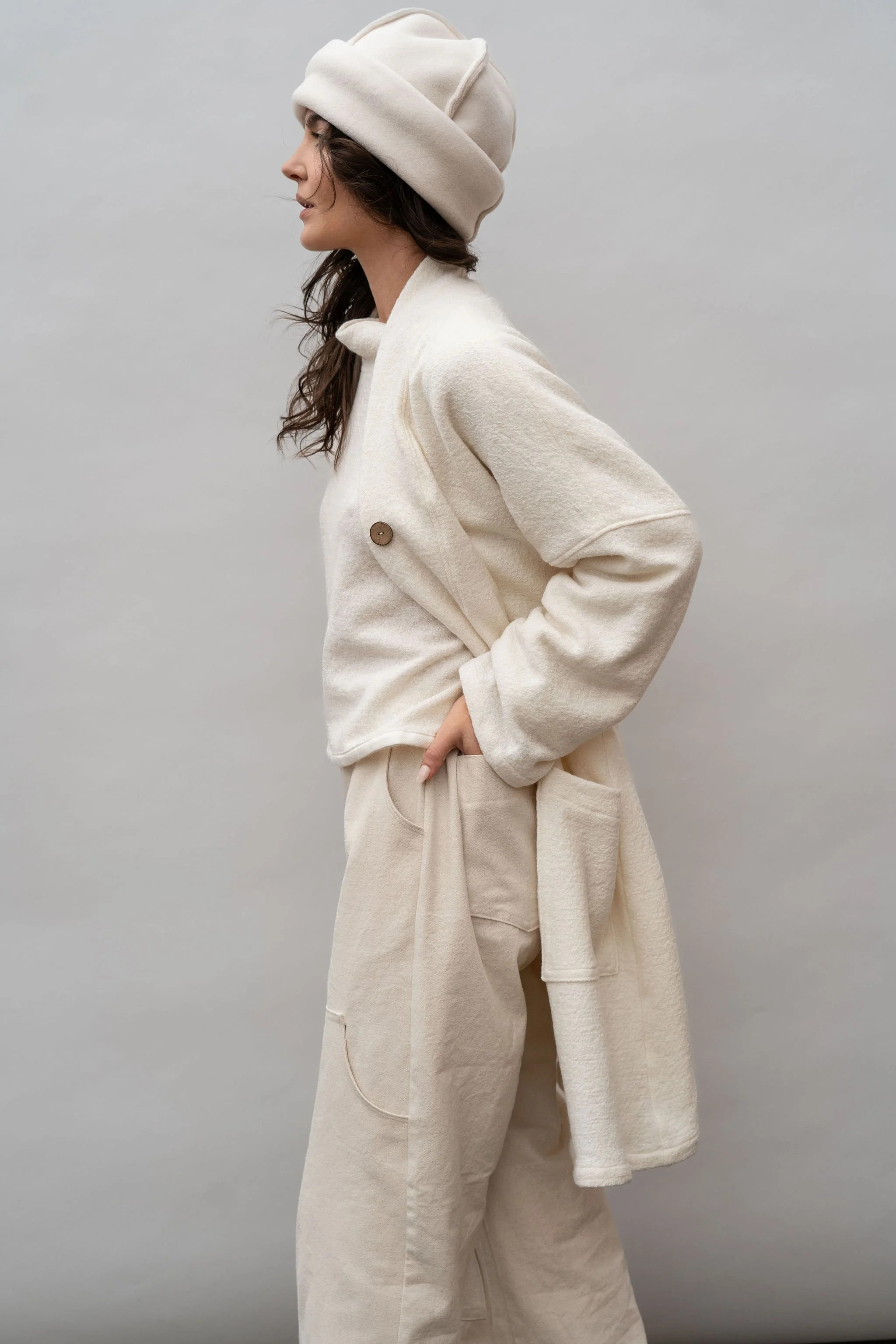 Side view of a woman wearing a wool coat in Vanilla facing left with hands in back pockets