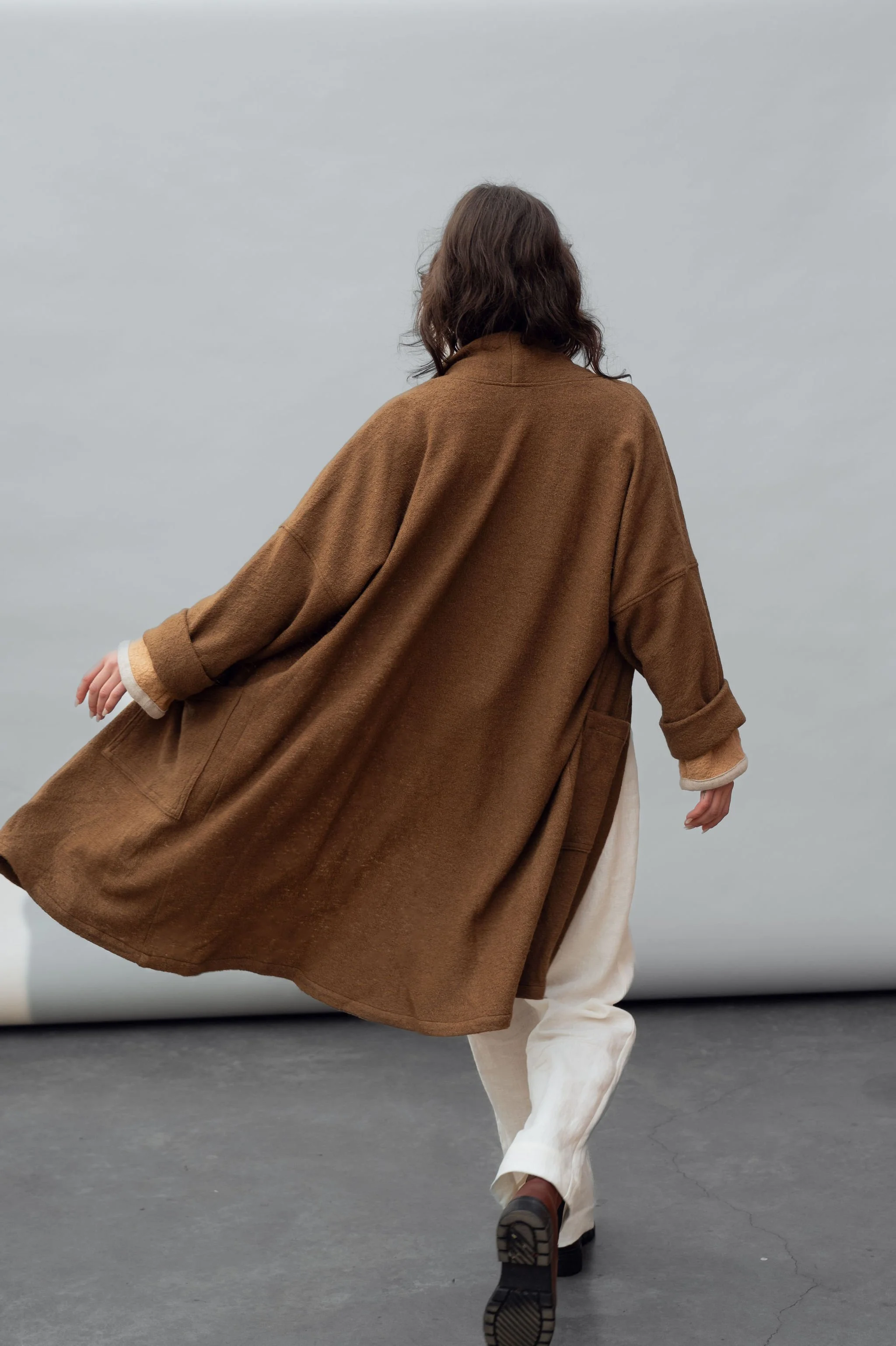 Back view of a woman wearing a wool coat in Bark and white pants walking