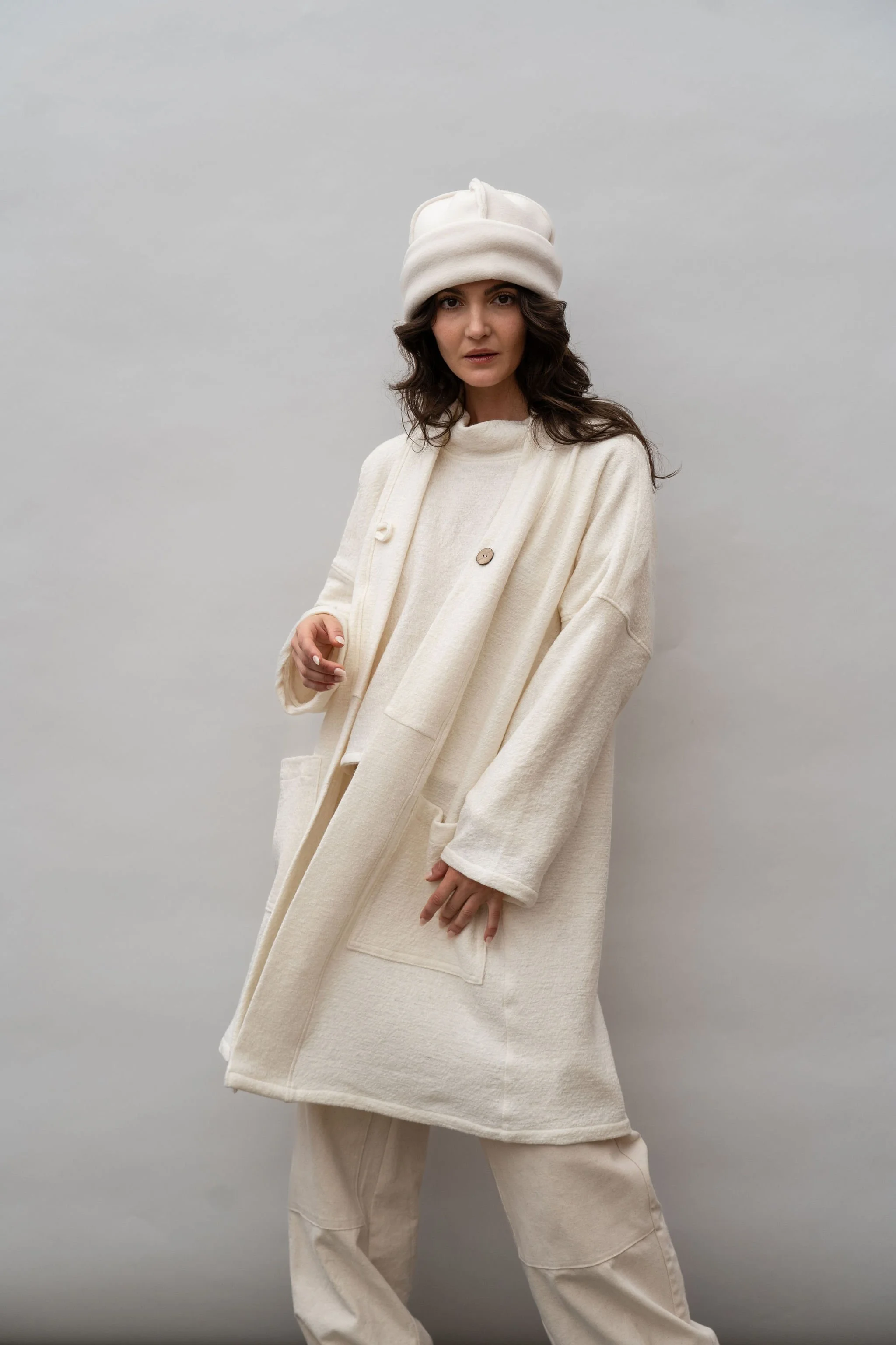 Front view of a woman wearing a wool coat in Vanilla and pointing