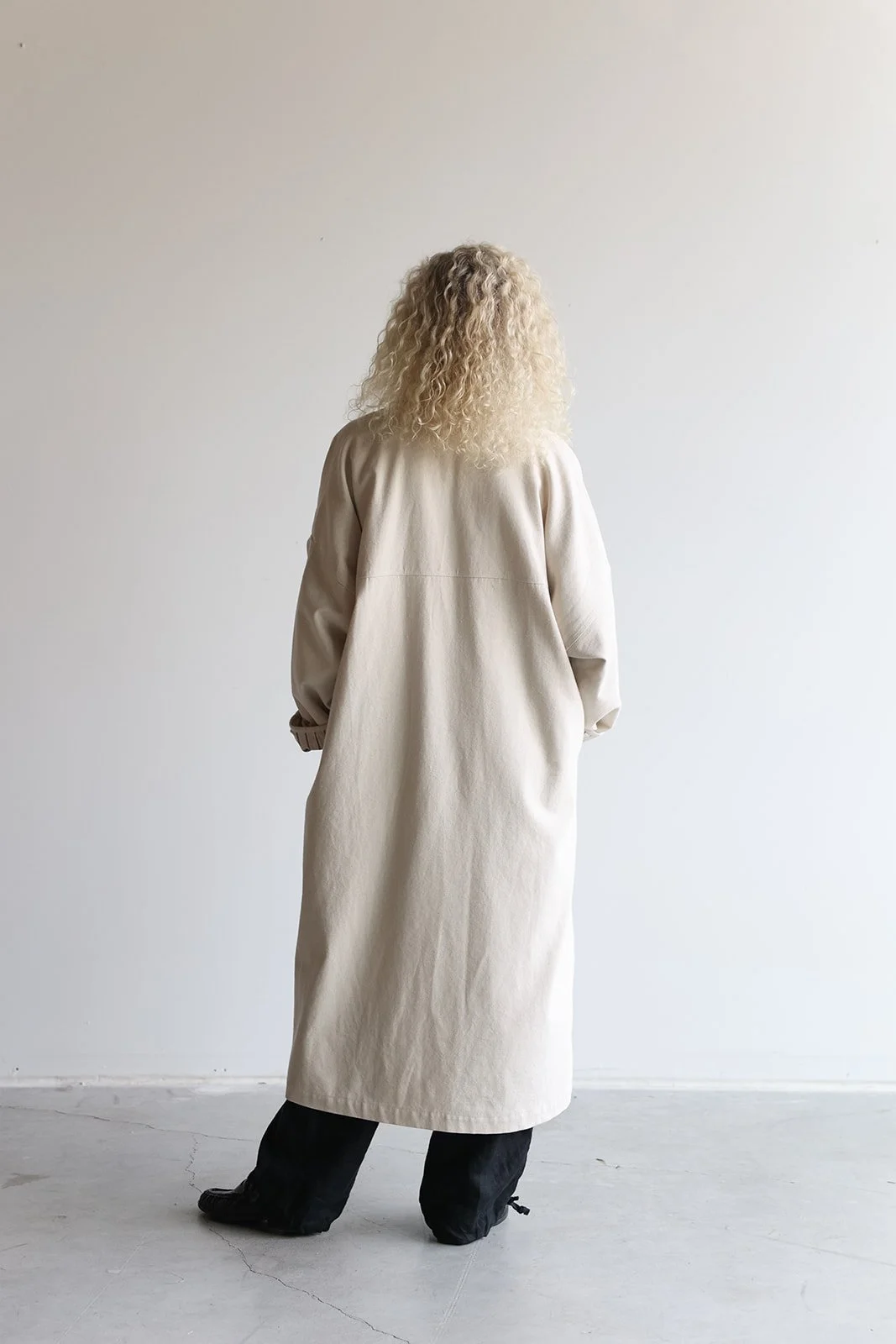 Back view of a woman wearing a canvas linen trench coat in Sand with hands in pockets
