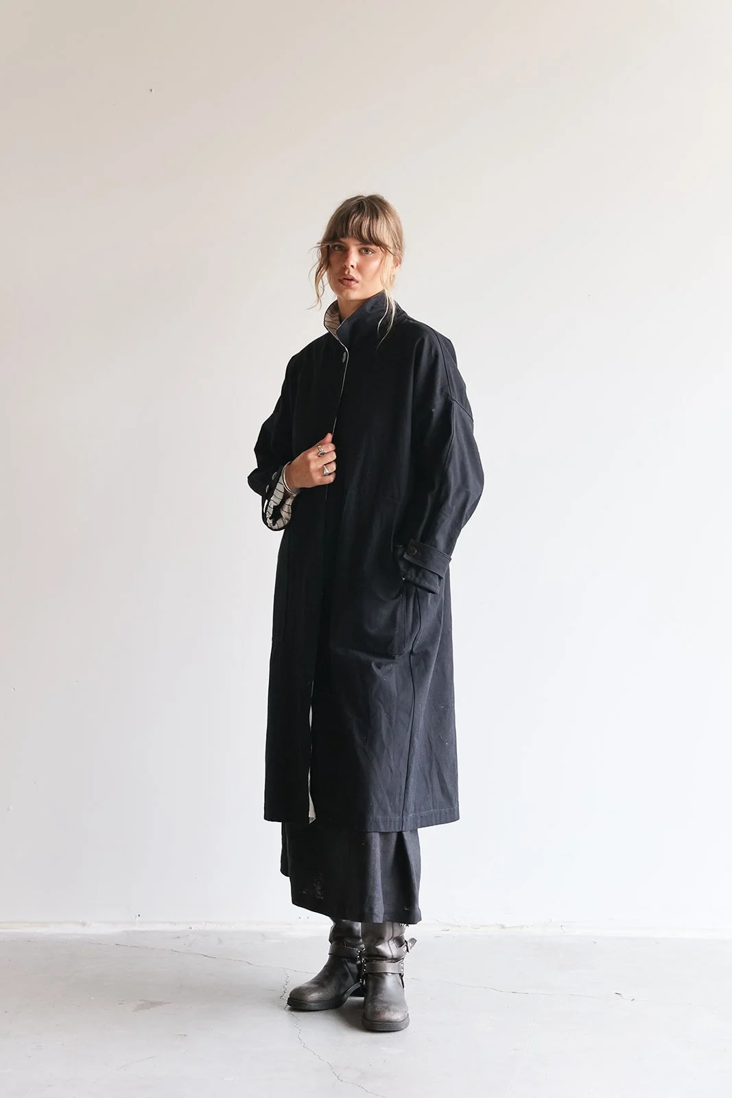 Front view of a woman wearing a canvas linen trench coat in holding onto coat