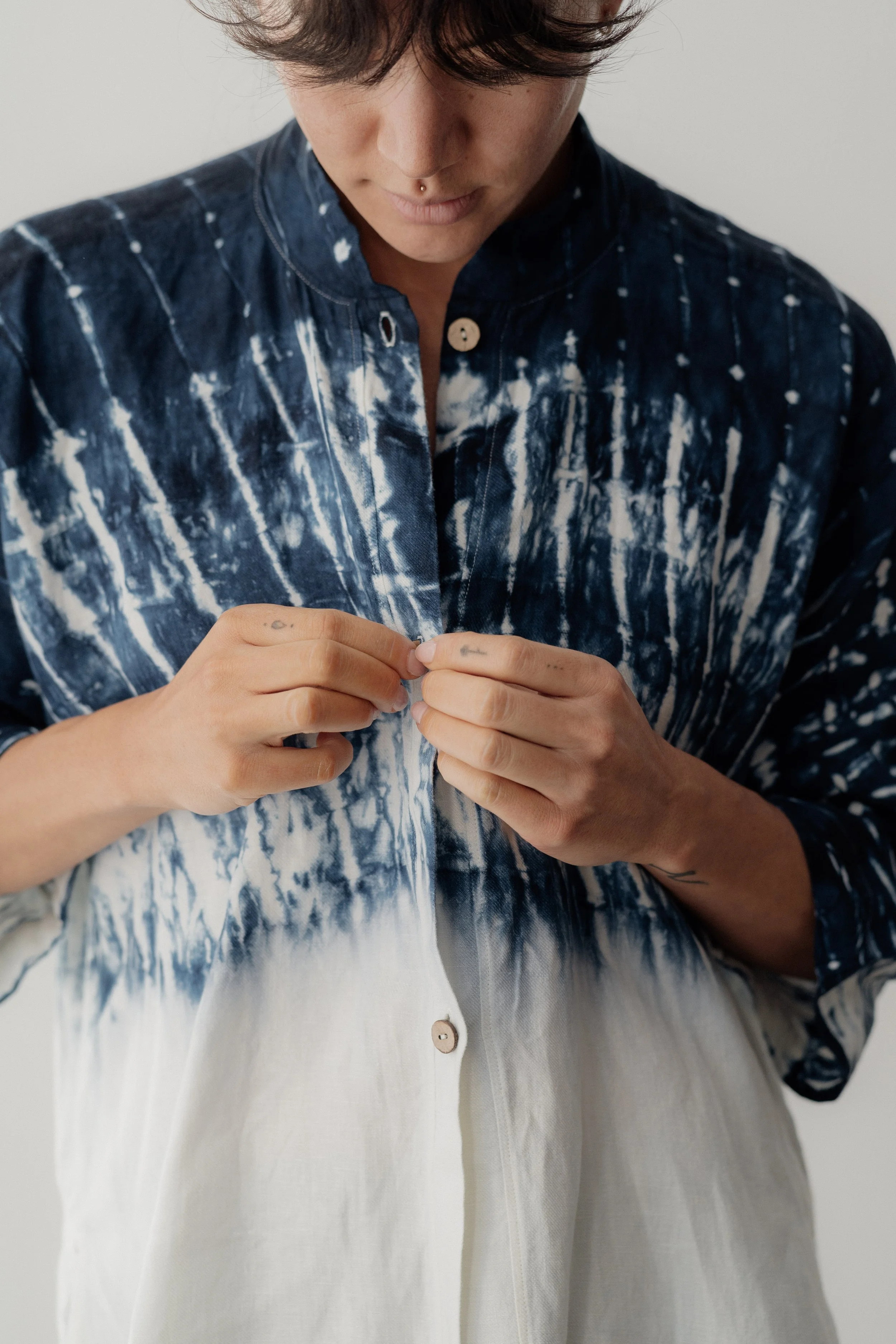 Person buttoning a white and blue tie-dye shirt with a standing collar.