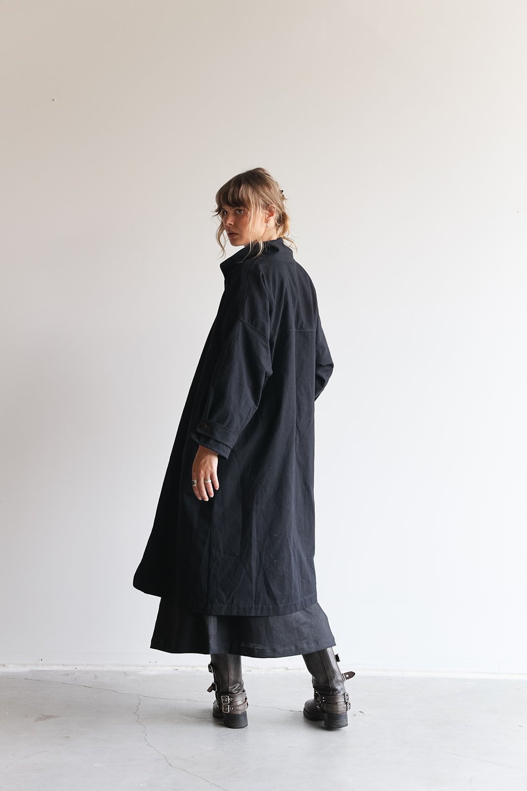 Back view of a woman wearing a canvas linen trench coat in Black looking over the left shoulder
