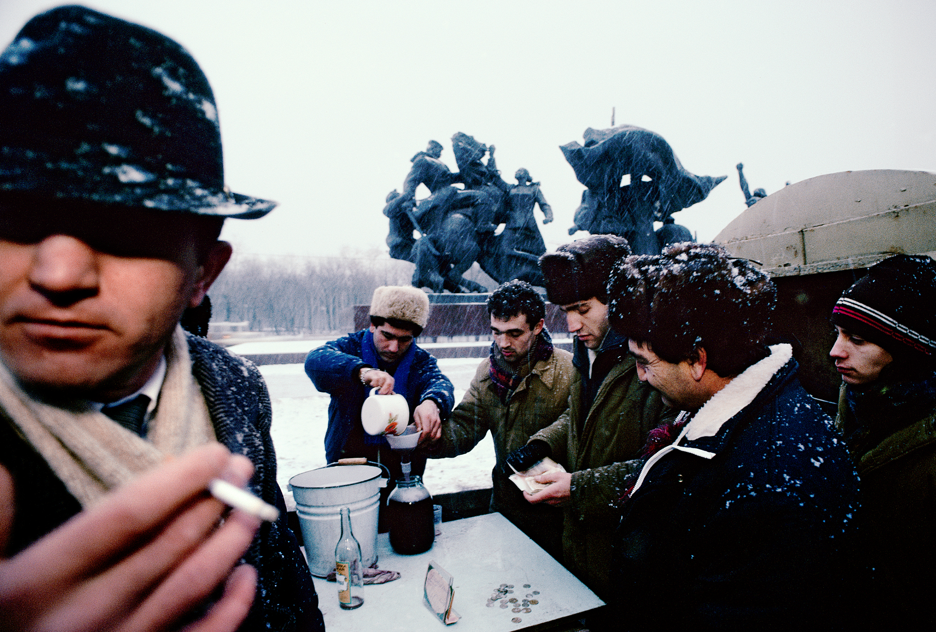  A smoking sentry stands guard as his partners sell shots of homemade wine to thirsty Muscovites. With the end of the Soviet era, these moonshiners from the Caucasus were free to bring their business to the Russian capital.  Moscow, Russia  