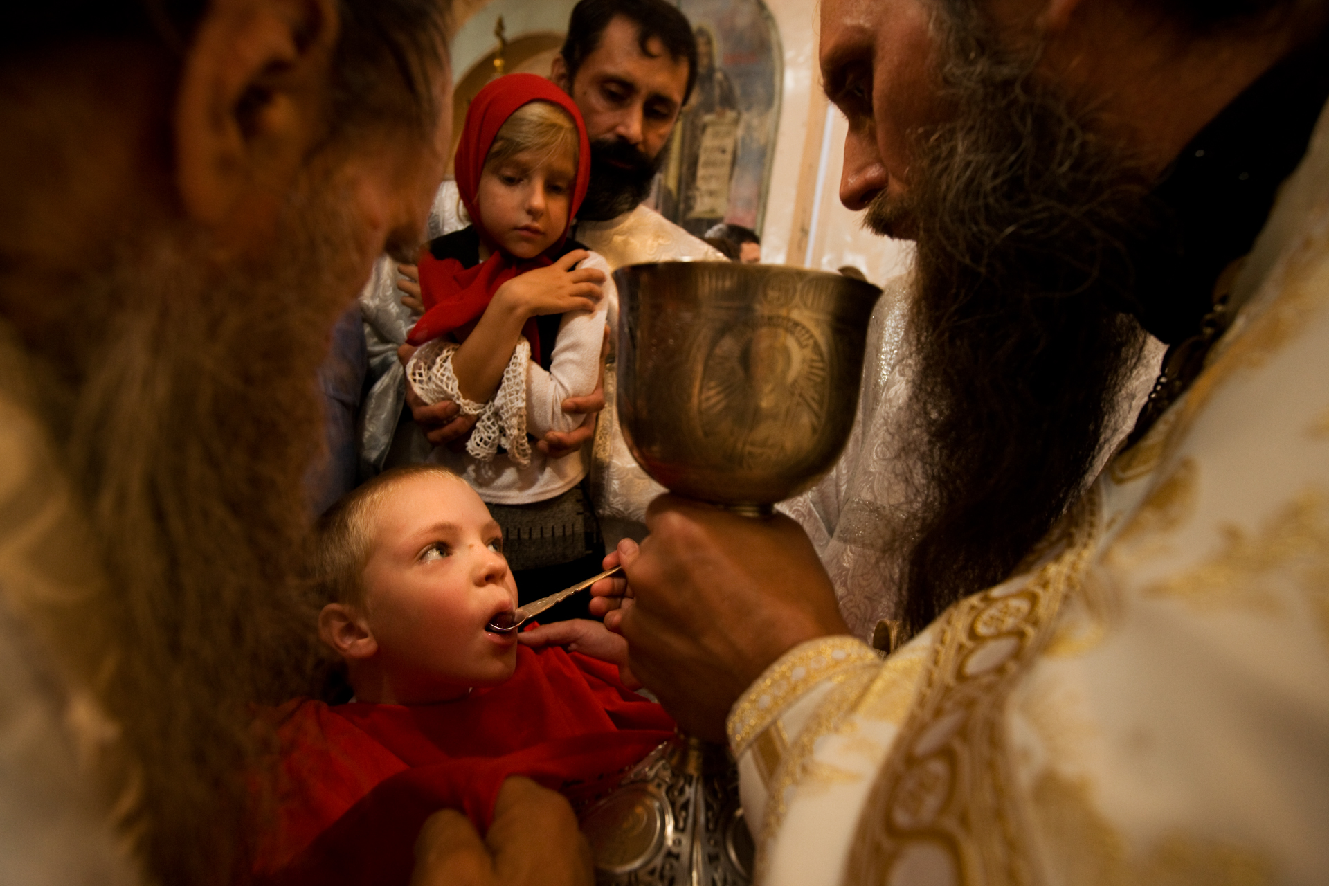  For an early taste of religion, a child receives Communion wine from Father Sergy at the Znamensky Cathedral.  Tyumen, Russia  