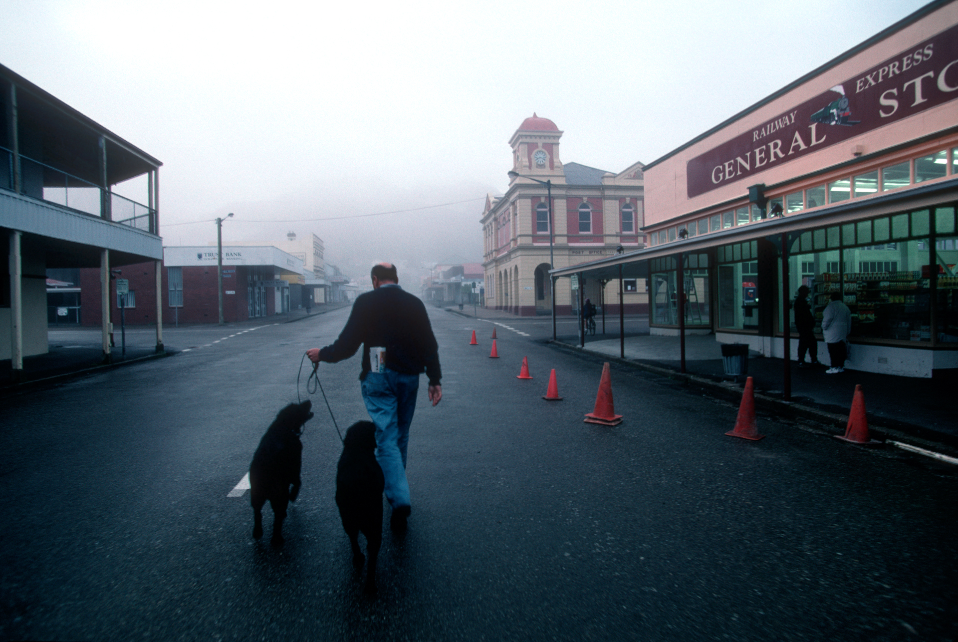  Heading for the coffeshop with dogs on the leash, a pedestrian crosses Main Street in early morning mist.  Queenstown  