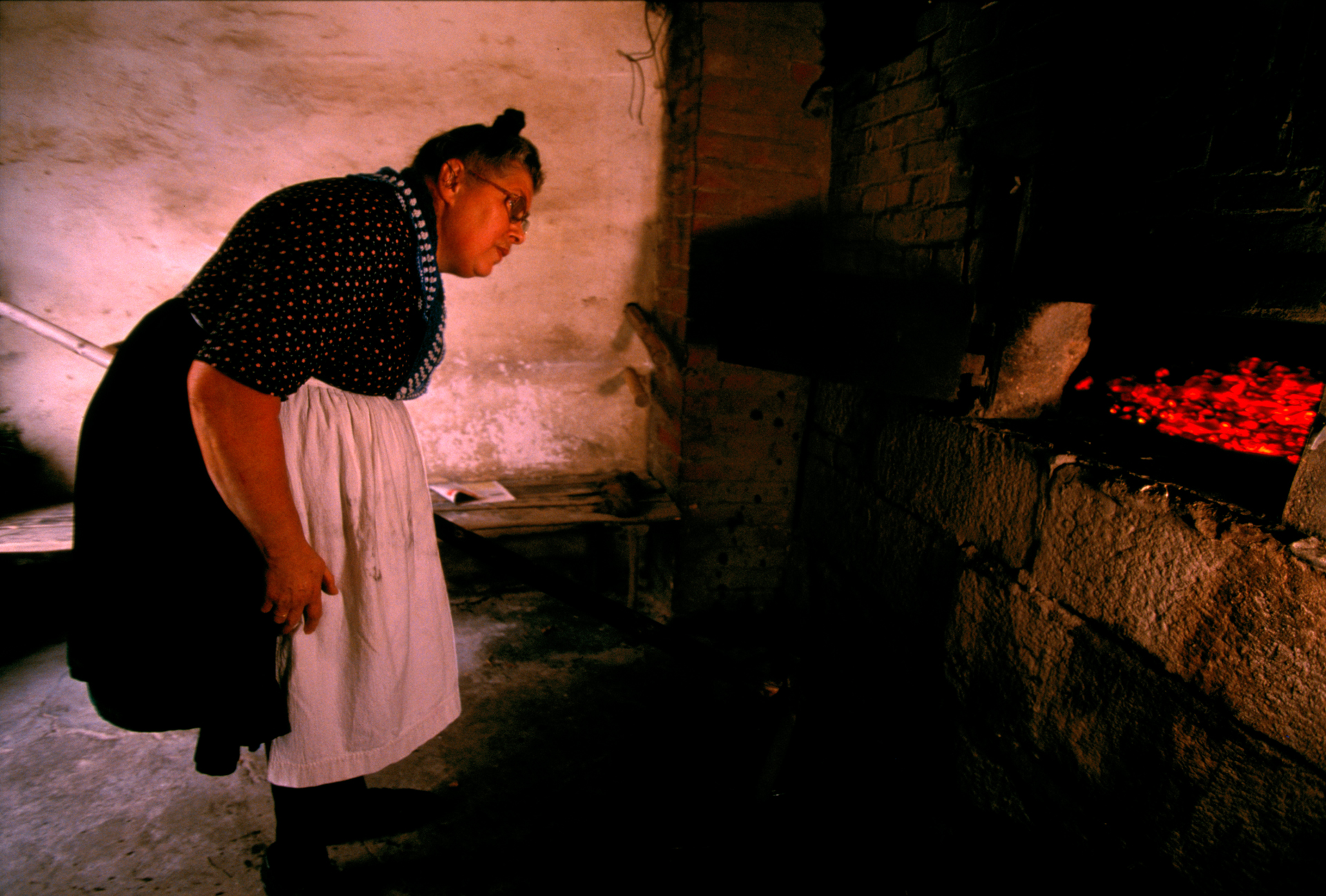  A villager peers into the fiery mouth of the communal oven.  Röllshausen, Germany  