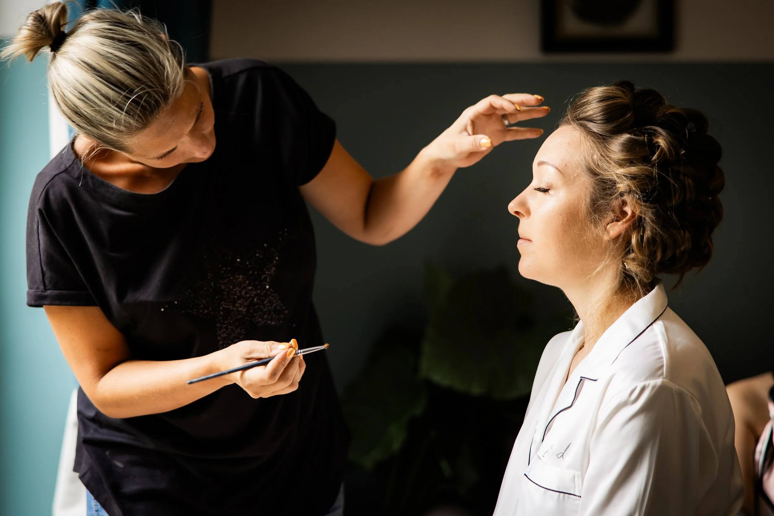 Makeup artist applying makeup to a woman's face with closed eyes.