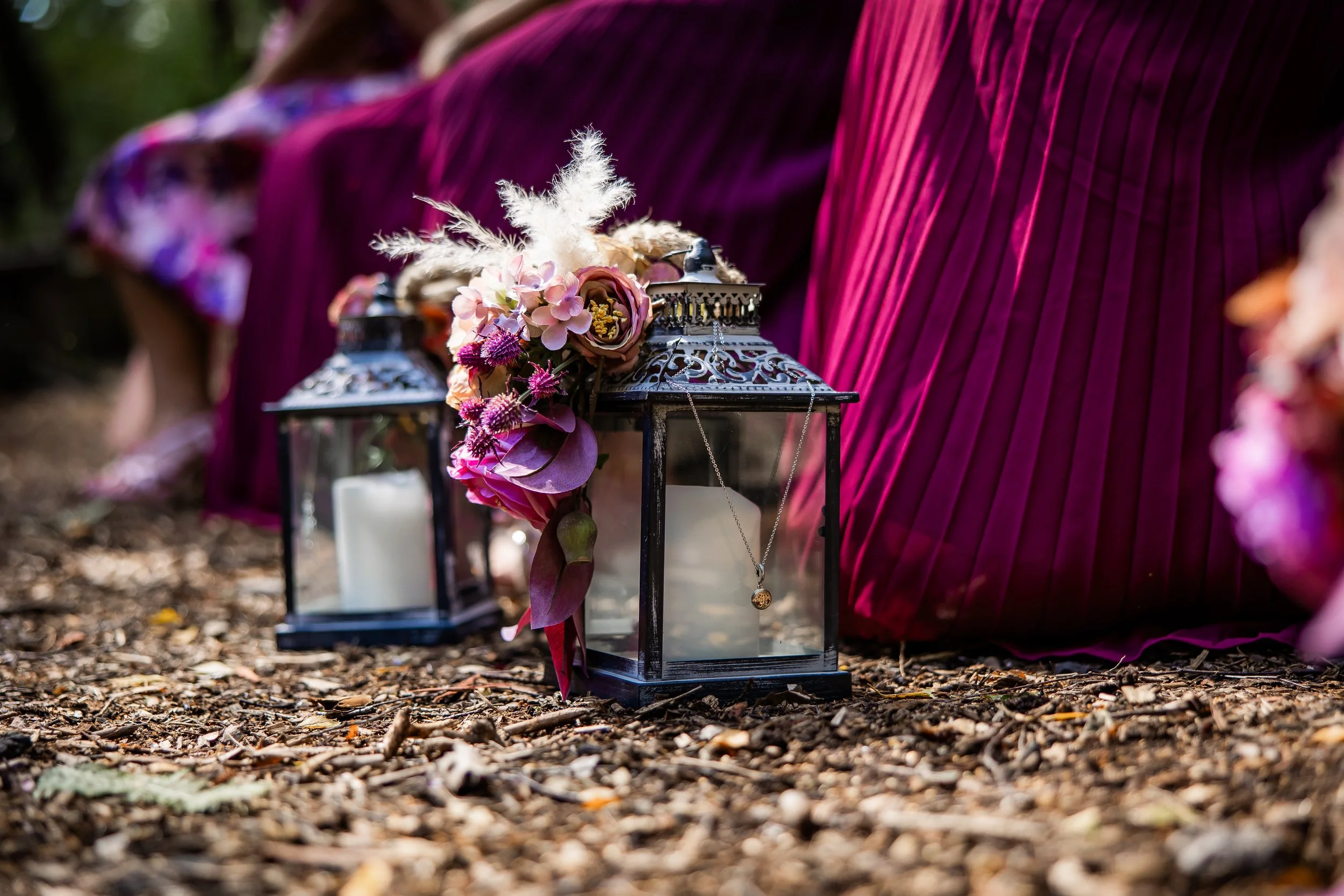 Decorative lanterns with candles and floral arrangements on a wooded surface at an outdoor event.