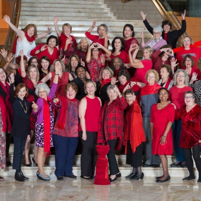 WomenHeart Champions, about 60 women, many in red, stand on a large staircase cheering and waving.