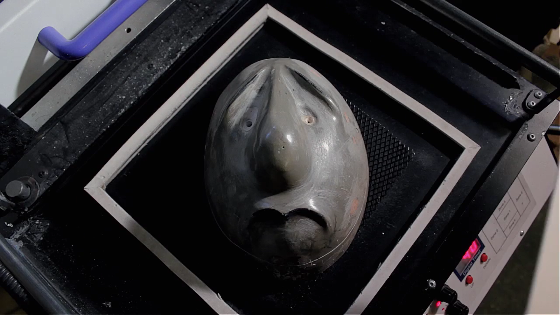 3) The mask mould is placed into the vacuum former and the tray is lowered. We place the sheet of 2mm HIPS plastic into the machine and secure it in place checking that there is an air tight fit We remove the heating element and raise the tray with the board on and turn on the vacuum pump.