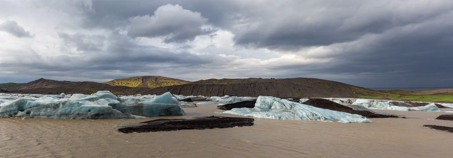 Svínafellsjökull glacier lagoon in Iceland with blue and black ice floating in brown water