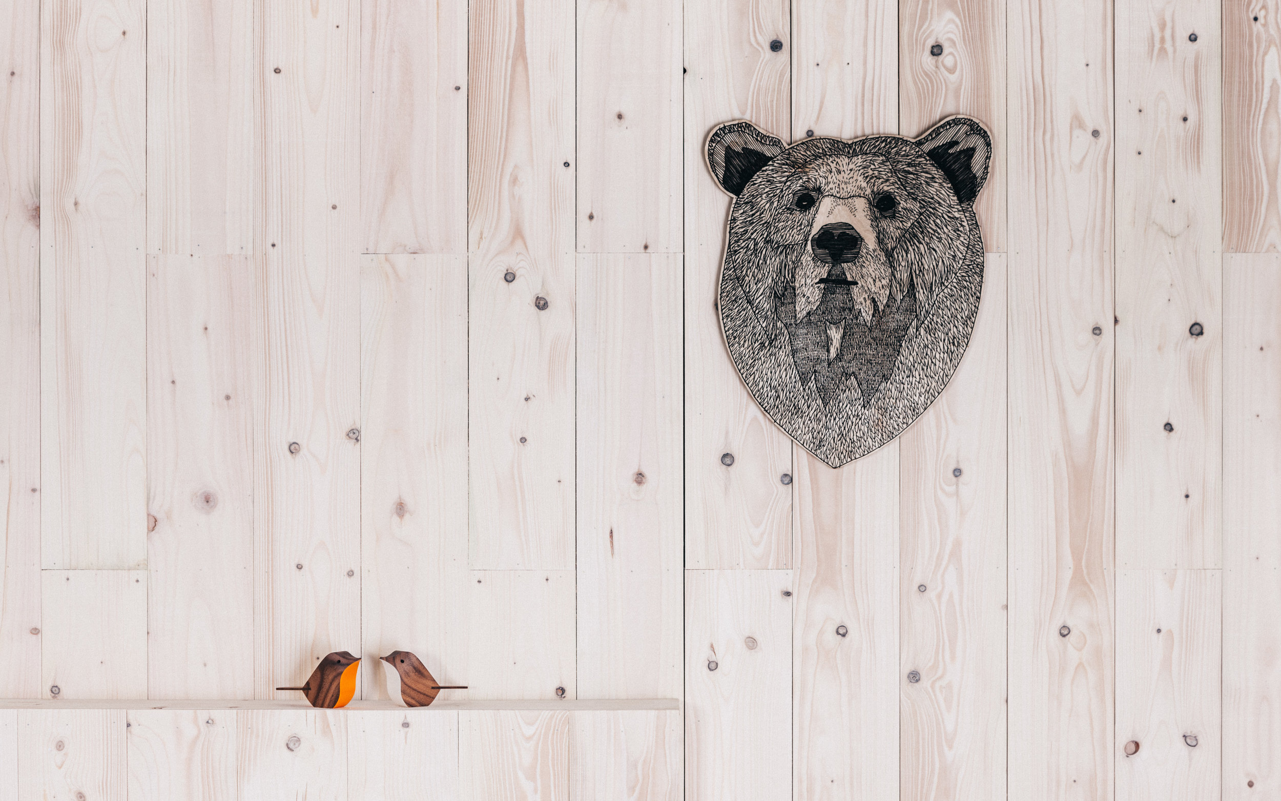 Illustration of a bears head on a piece of plywood, next to two small wooden birds.