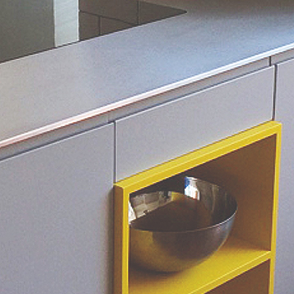Custom designed Island unit for a contemporary kitchen. It has  a stainless steal worktop with an inset  induction hob. The doors are grey and there is some open shelving painted yellow.