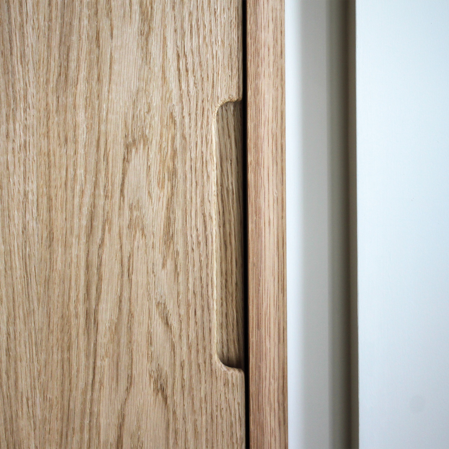 Close up image of a finger pull handle on a large pair of Oak wooden sliding doors, on this bespoke fitted coat cupboard. 