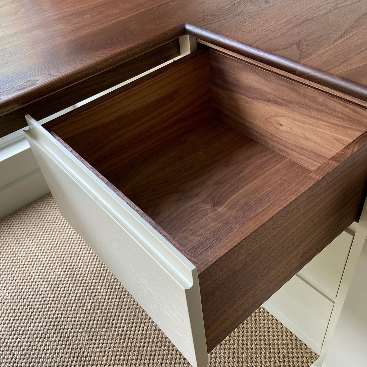 Drawer box made from walnut wood with a white painted front. The drawer is open and extending out from under a solid walnut desk. 
